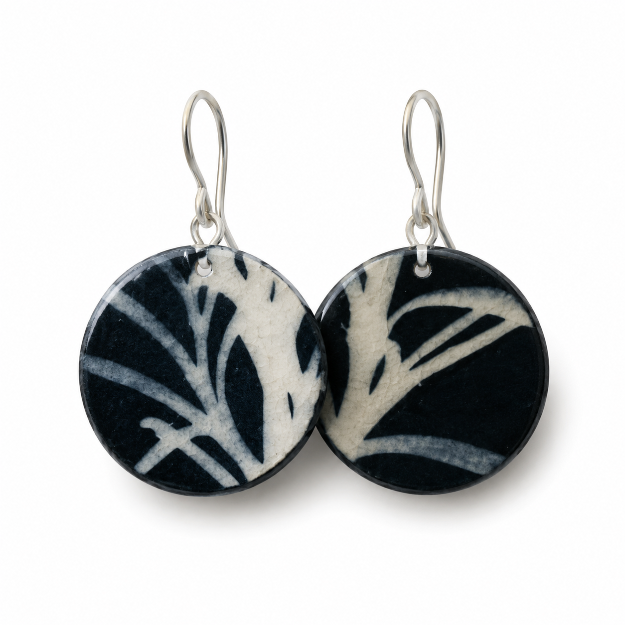 A pair of round black and white patterned dangle earrings with silver fishhook wires, shown against a plain white background.