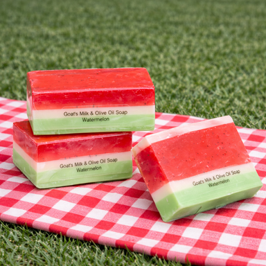 Perfect Summer Watermelon Soaps by The Grecian Soap Company, featuring three colorful soap bars shaped like watermelon wedges, showcasing a creamy goat's milk and olive oil formula on a checkered cloth.