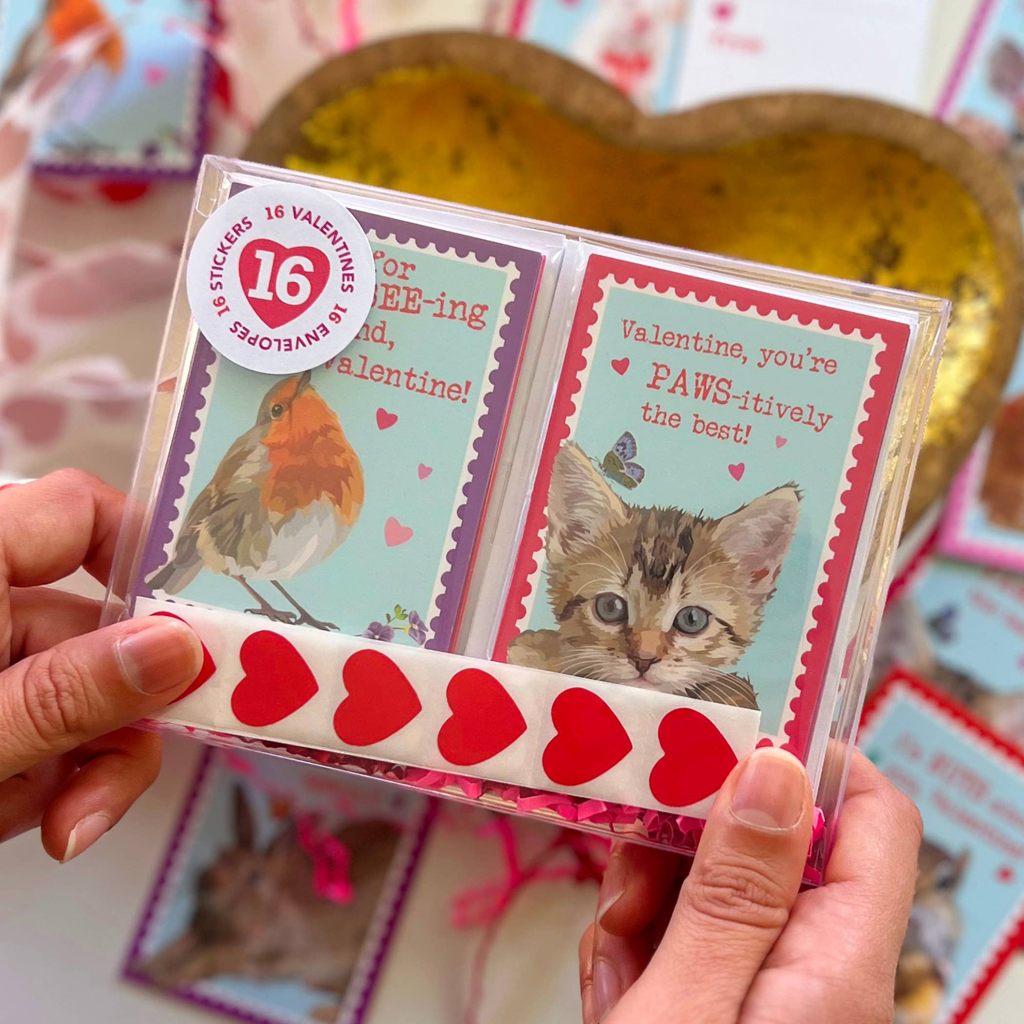 Boxed Set of 16 Kids Valentines Cards Kit by The Red Barn Press, featuring adorable animal-themed Valentine cards and heart stickers. Hands holding the clear acrylic box showcasing two card designs, perfect for kids.