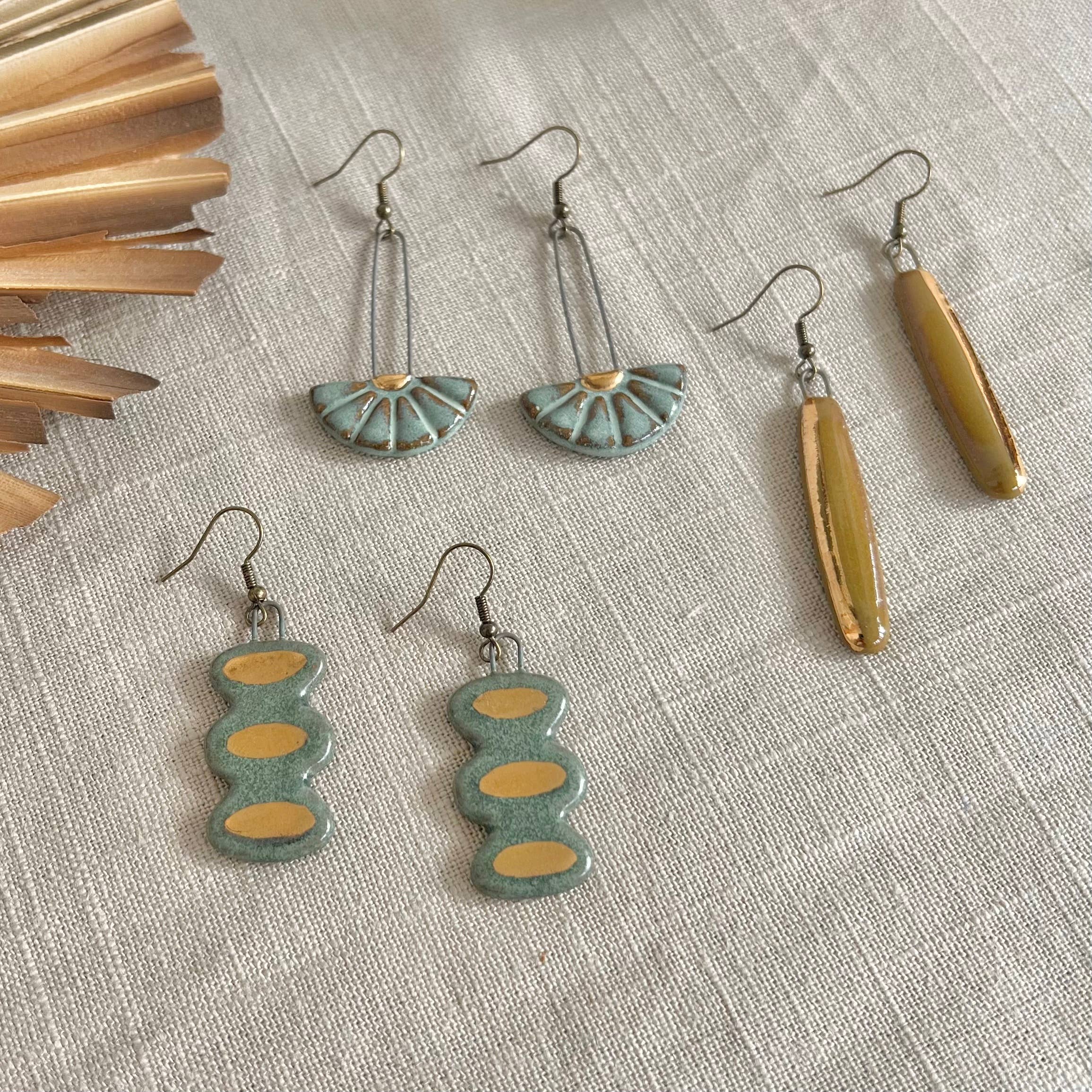 Collection of Turquoise Sun Burst Ceramic Earrings by The Artifact House featuring various designs, including sunburst and gold-accented styles, arranged on a neutral fabric background.