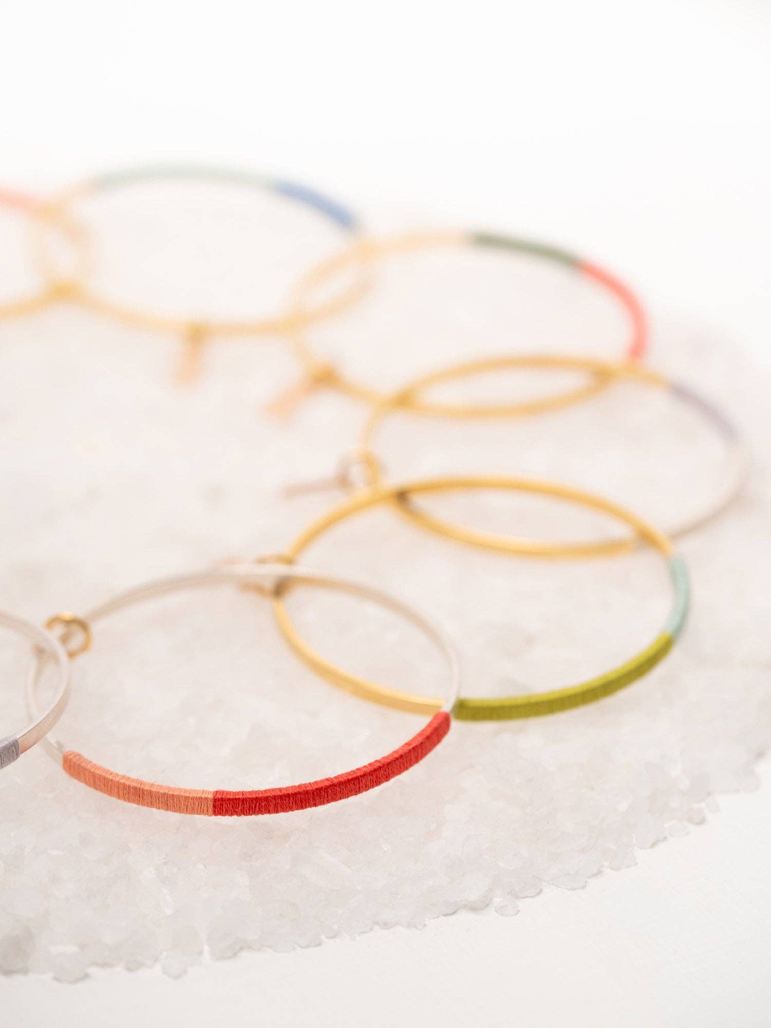 Colorful Gold Wrapped Circle Bangles by Twenty Two West displayed on a textured white surface, showcasing an array of vibrant hues and 24k gold plated details.