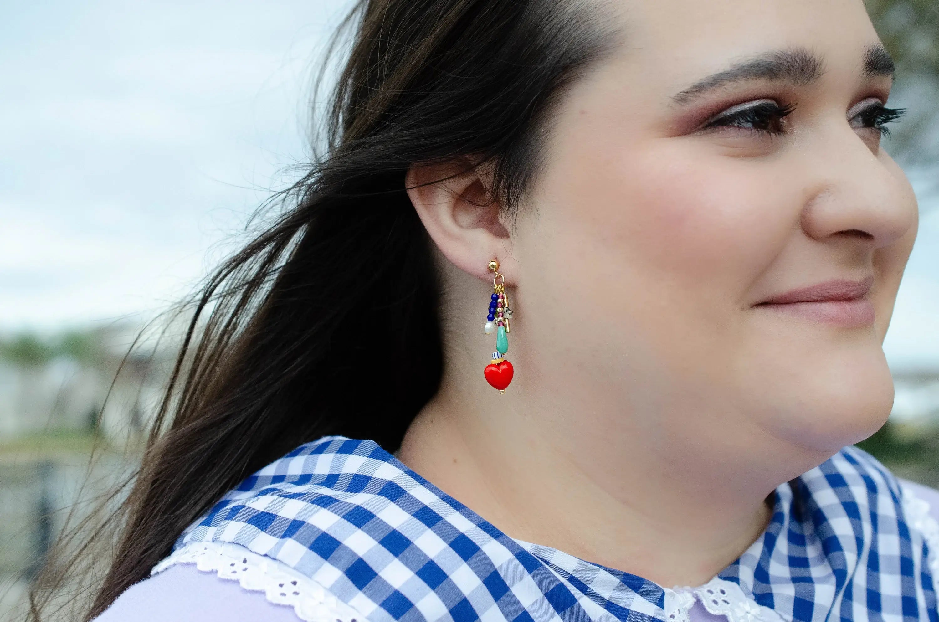 Woman wearing Heart Charm Earrings by Jill Makes, highlighting the colorful design with red heart charms and assorted beads, captured outdoors with natural light.