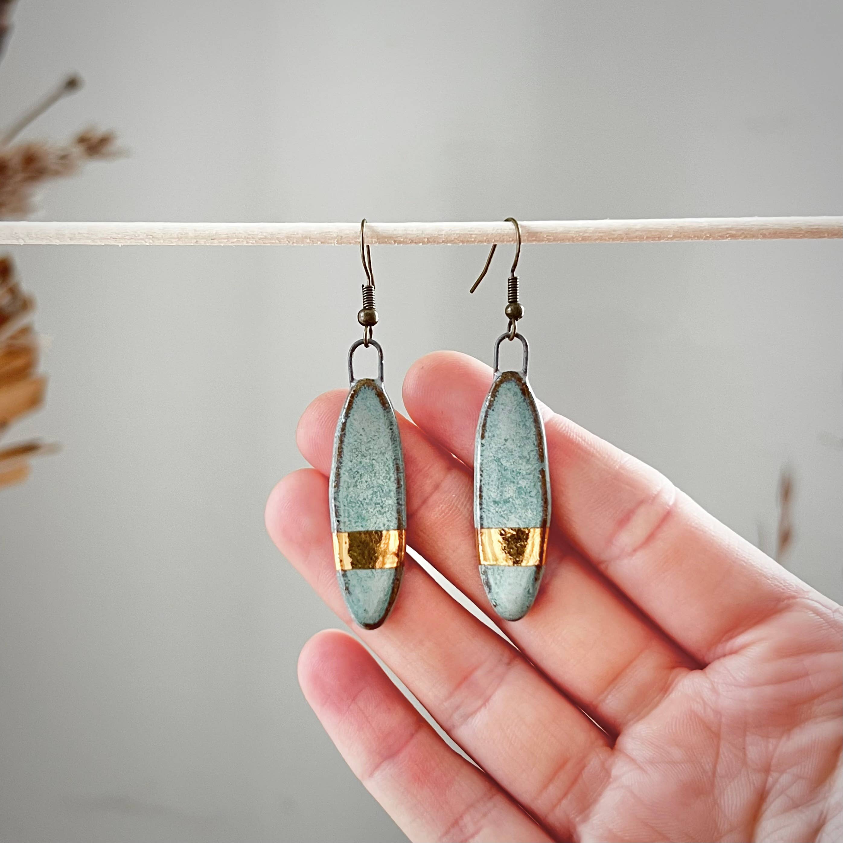 A close-up of Turquoise with Solid Gold Striped Earrings from The Artifact House held in hand, emphasizing the elegant craftsmanship and color.