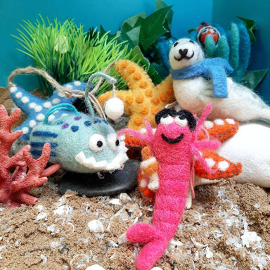 Colorful felt sea creature ornaments on a sandy surface with plants and rocks.
