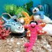 Colorful felt sea creature ornaments on a sandy surface with plants and rocks.