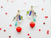 Colorful Heart Charm Earrings by Jill Makes featuring a cluster of colorful beads and a heart pendant, displayed against a white background with red sequins.