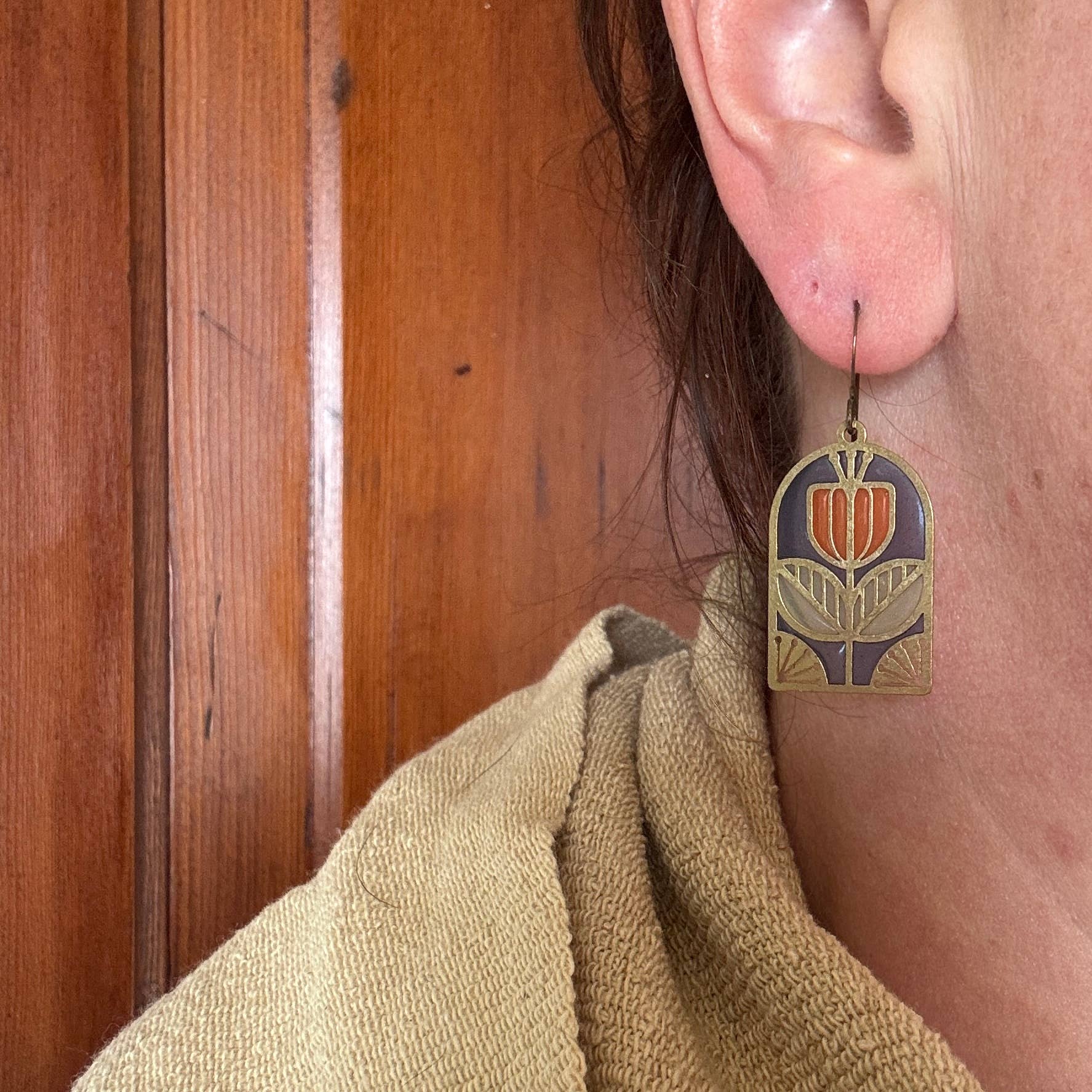 Close-up of a model wearing Tracery Stained Glass Resin Earrings by Wild Lupine Folkcraft, featuring a detailed view of the brass and resin design hanging from the ear, demonstrating elegance and style.