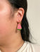 Close-up view of a person wearing Mini Watermelon Dangle earrings by Sunnie Creative, emphasizing the vibrant pink and green colors of the handmade earrings against a neutral background.