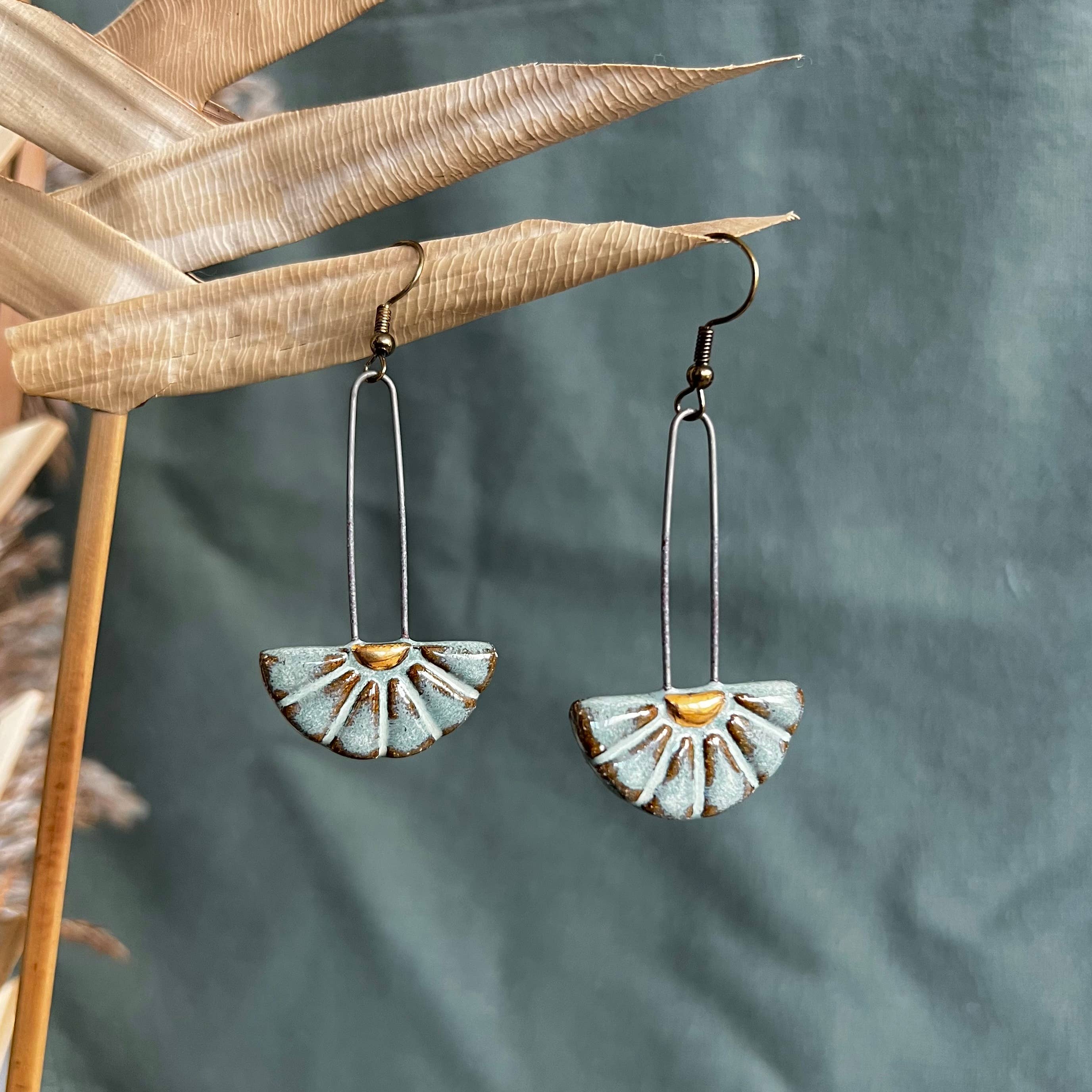 Turquoise Sun Burst Ceramic Earrings by The Artifact House featuring a modern design, suspended against a textured backdrop for added contrast.
