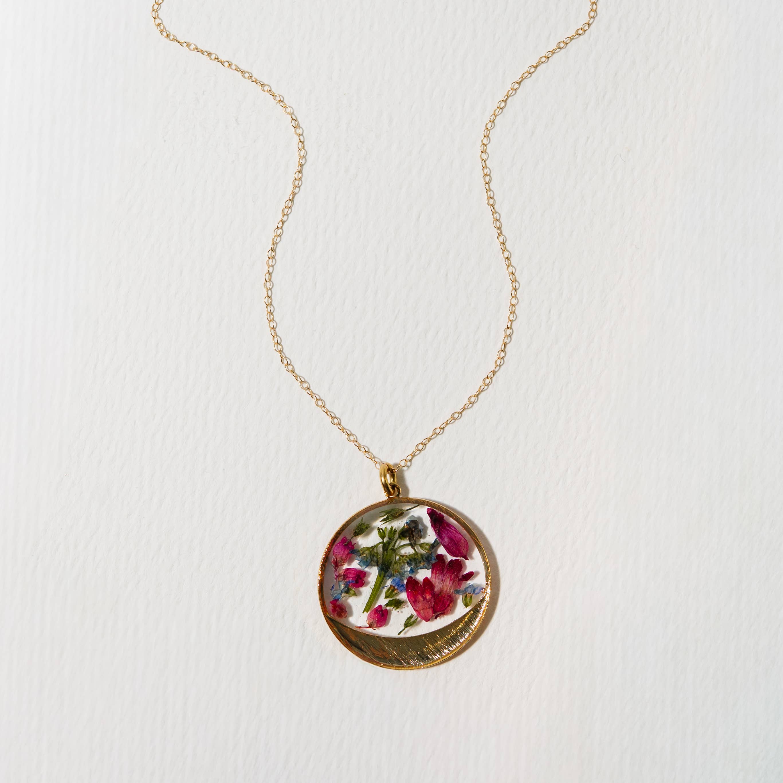 Garden Variety Flower Confetti Gold Moon Necklace featuring an 18" 14kt gold filled chain, adorned with vibrant flowers like coral bells, boronia, heather, and forget me not, all framed in a beautiful gold plated moon design.