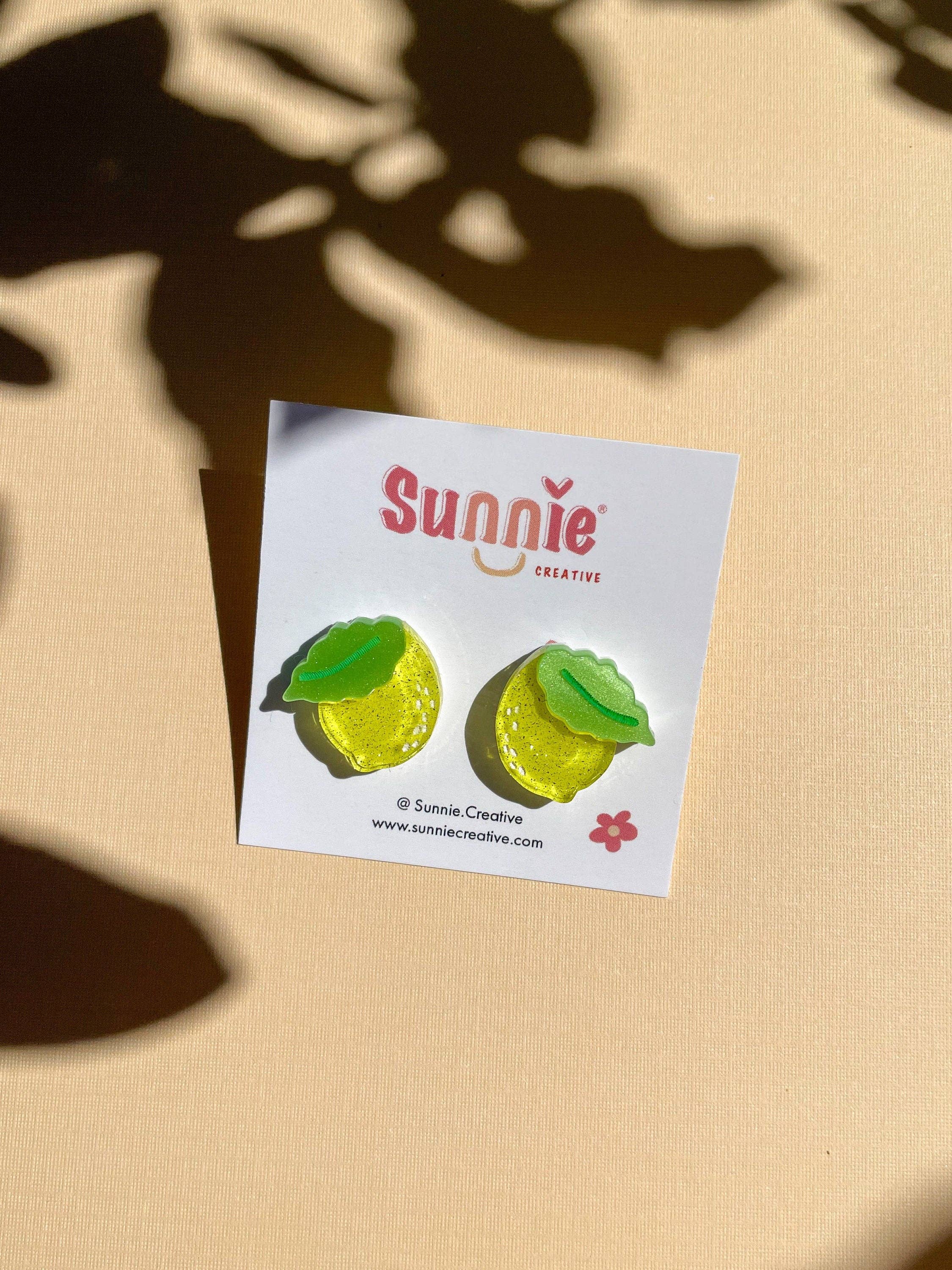 Mini Lemon Dangle earrings neatly arranged on a branded card by Sunnie Creative, emphasizing the bright yellow color and green leaf detail.