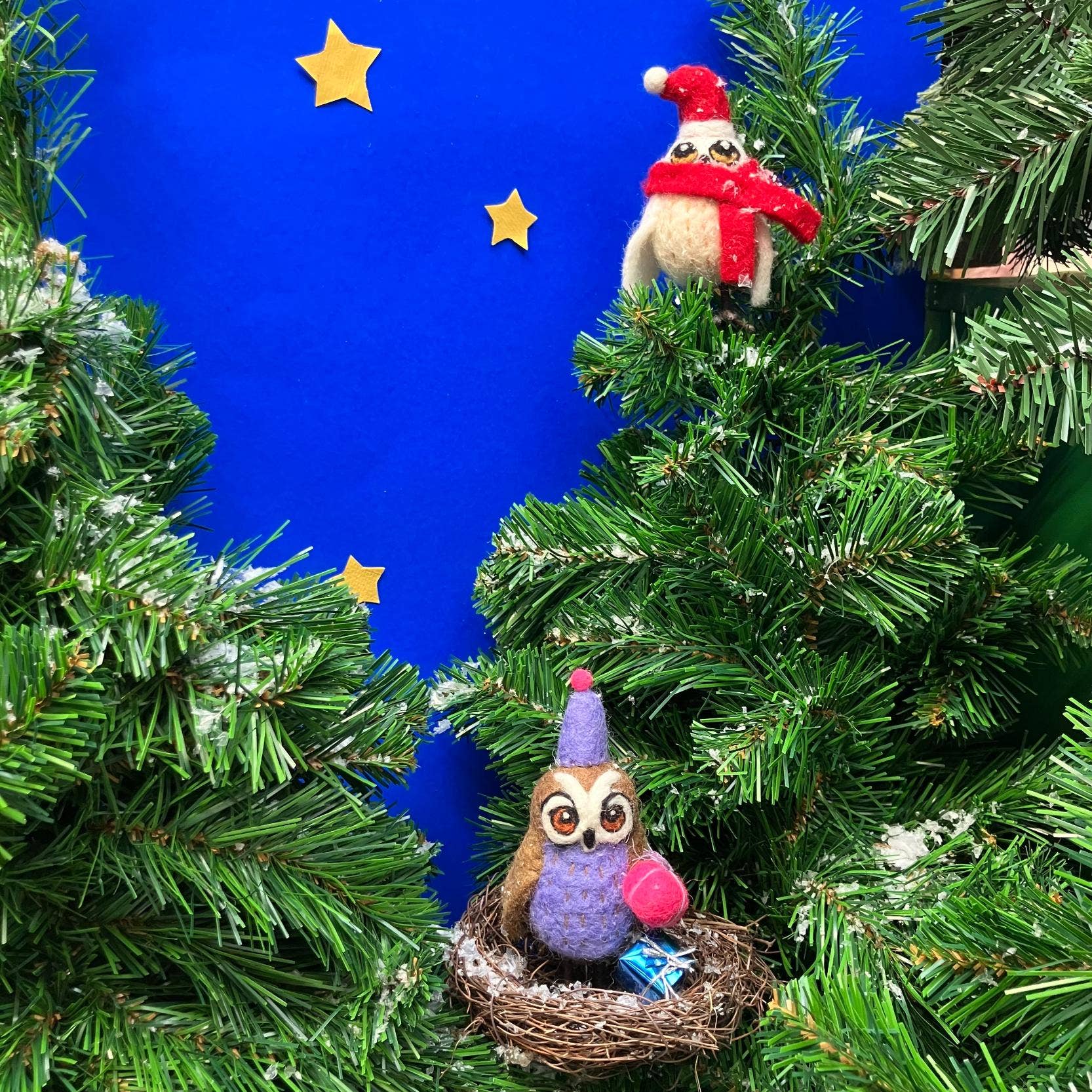 Felt owl ornaments in festive hats on a Christmas tree with a blue background