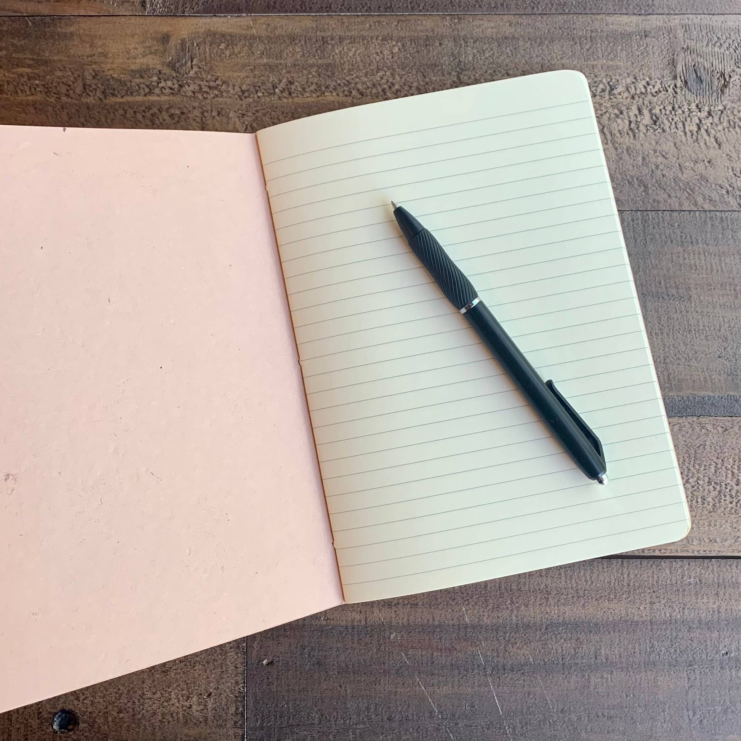 Open Softcover Notebook by The Casual Bookbinder, featuring lined pages and a black pen, ideal for writing and sketches.