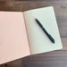 Open Softcover Notebook by The Casual Bookbinder, featuring lined pages and a black pen, ideal for writing and sketches.