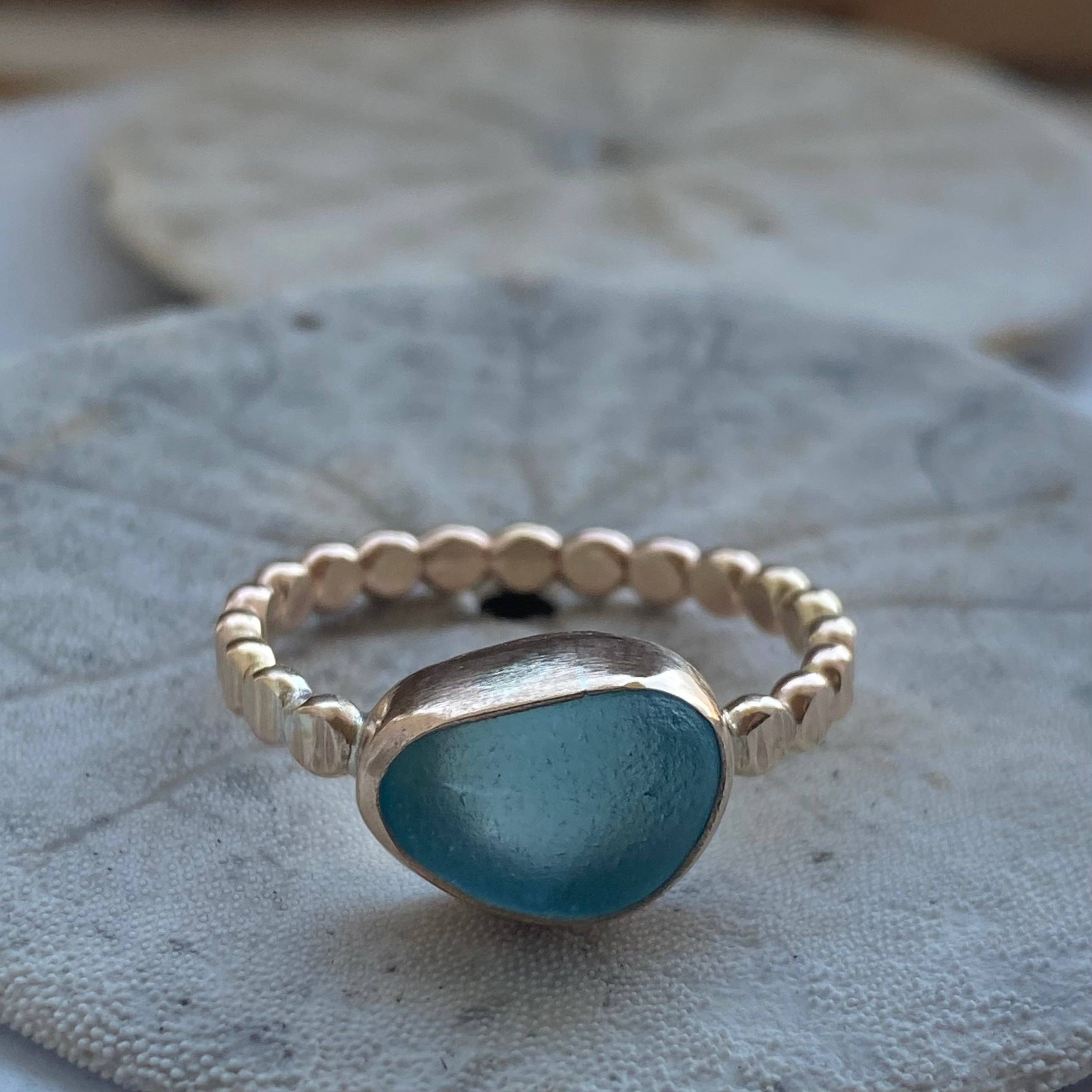 The Repetition Band | Sea Glass Ring by Kate Samson Design displaying a light aqua sea glass in a handcrafted bezel on a smooth textured gold band, set against a natural background.