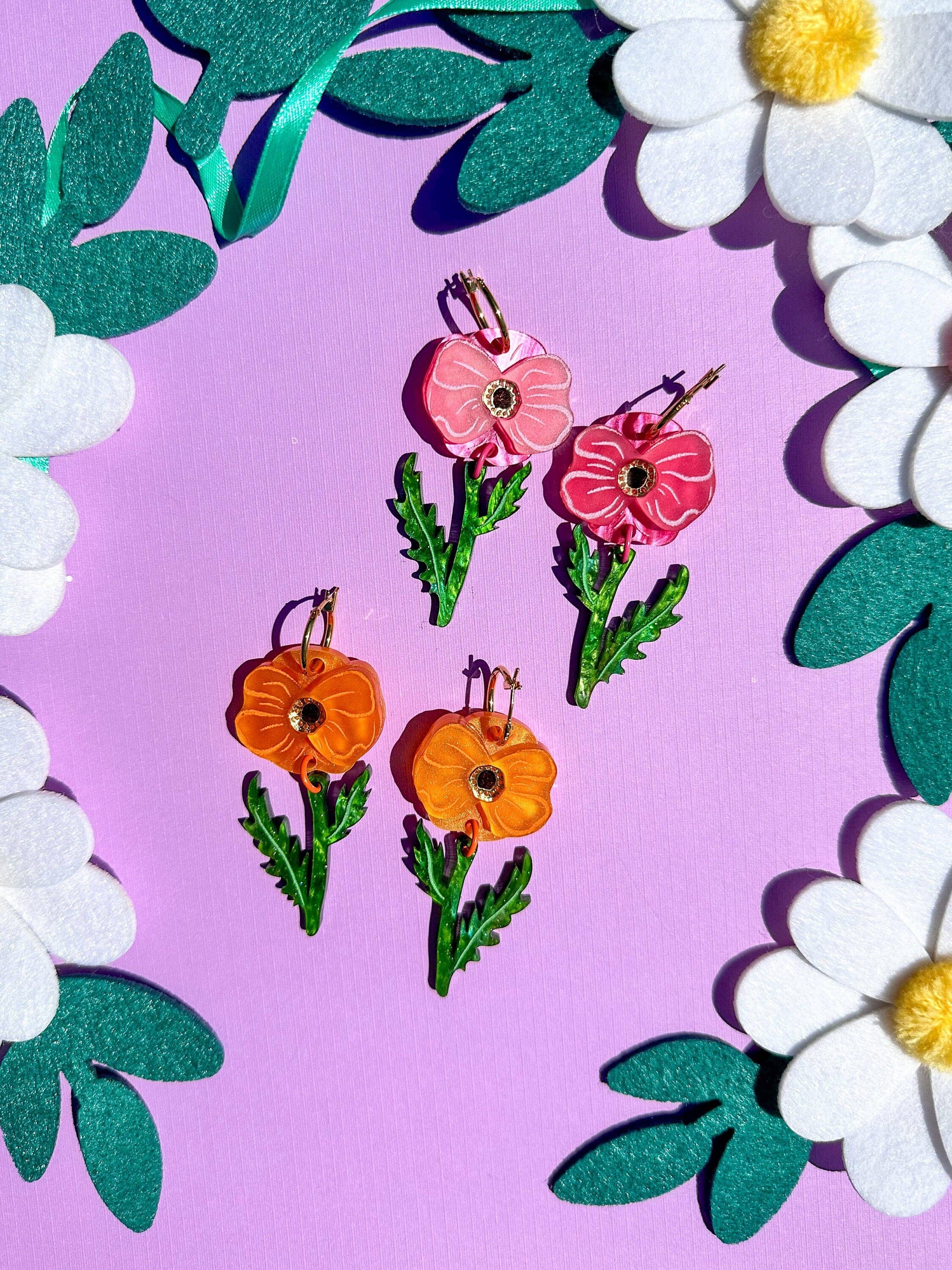Handmade Poppy Bloom flower earrings by Sunnie Creative featuring a vibrant assortment of pink and orange floral designs, set against a colorful background, showcasing their unique and bold aesthetic.