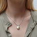 Model wearing the Small Button Necklace by Marjorie Baer, showcasing the brass and silver pendant on a silver snake chain.