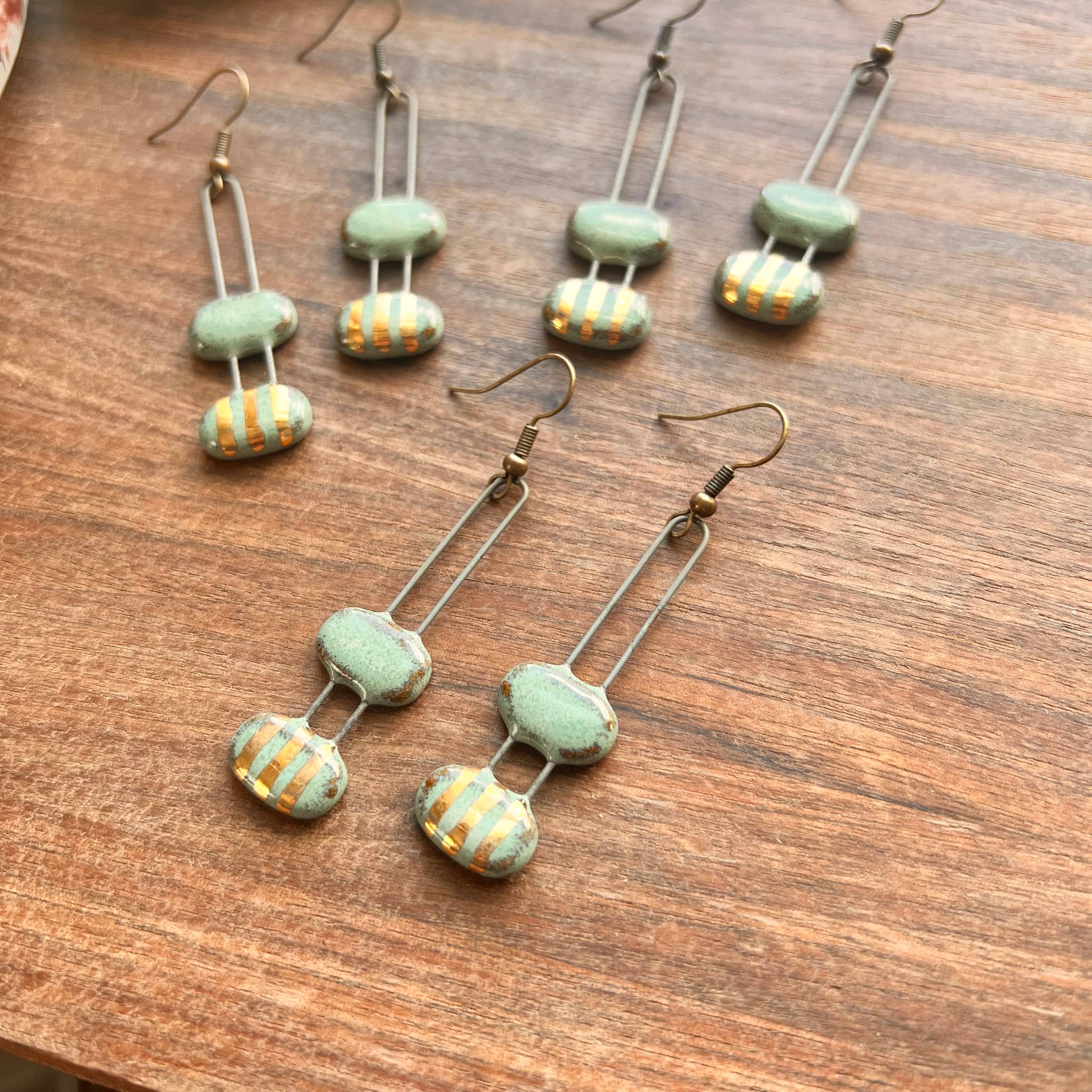 Close-up view of turquoise double bubble gold striped ceramic earrings by The Artifact House, showcasing their unique design and color on a rustic wooden background.
