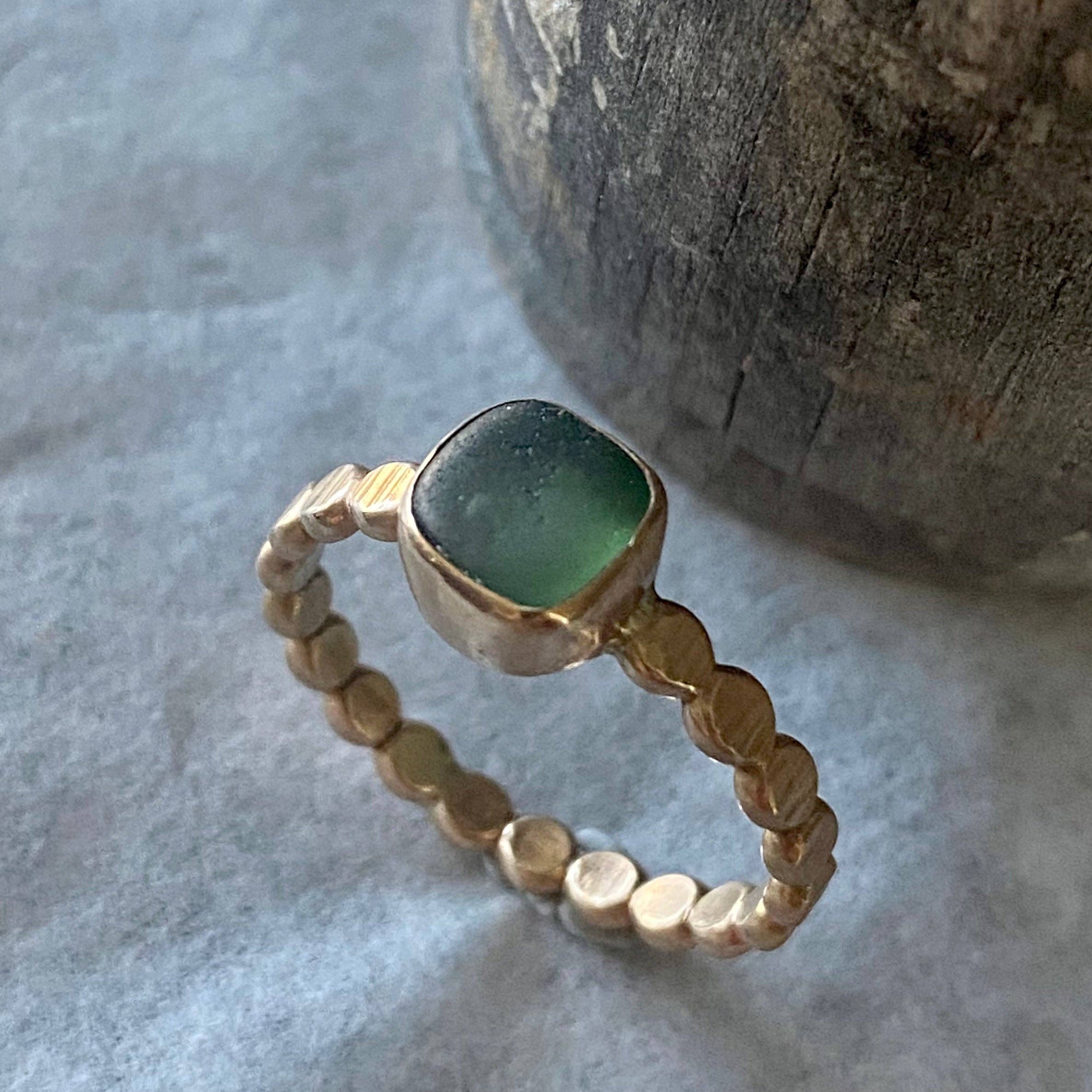 The Repetition Band | Sea Glass Ring by Kate Samson Design, displaying a stunning green sea glass set in a hand-crafted 14k gold fill bezel, highlighted on a textured surface with a focus on its unique design.