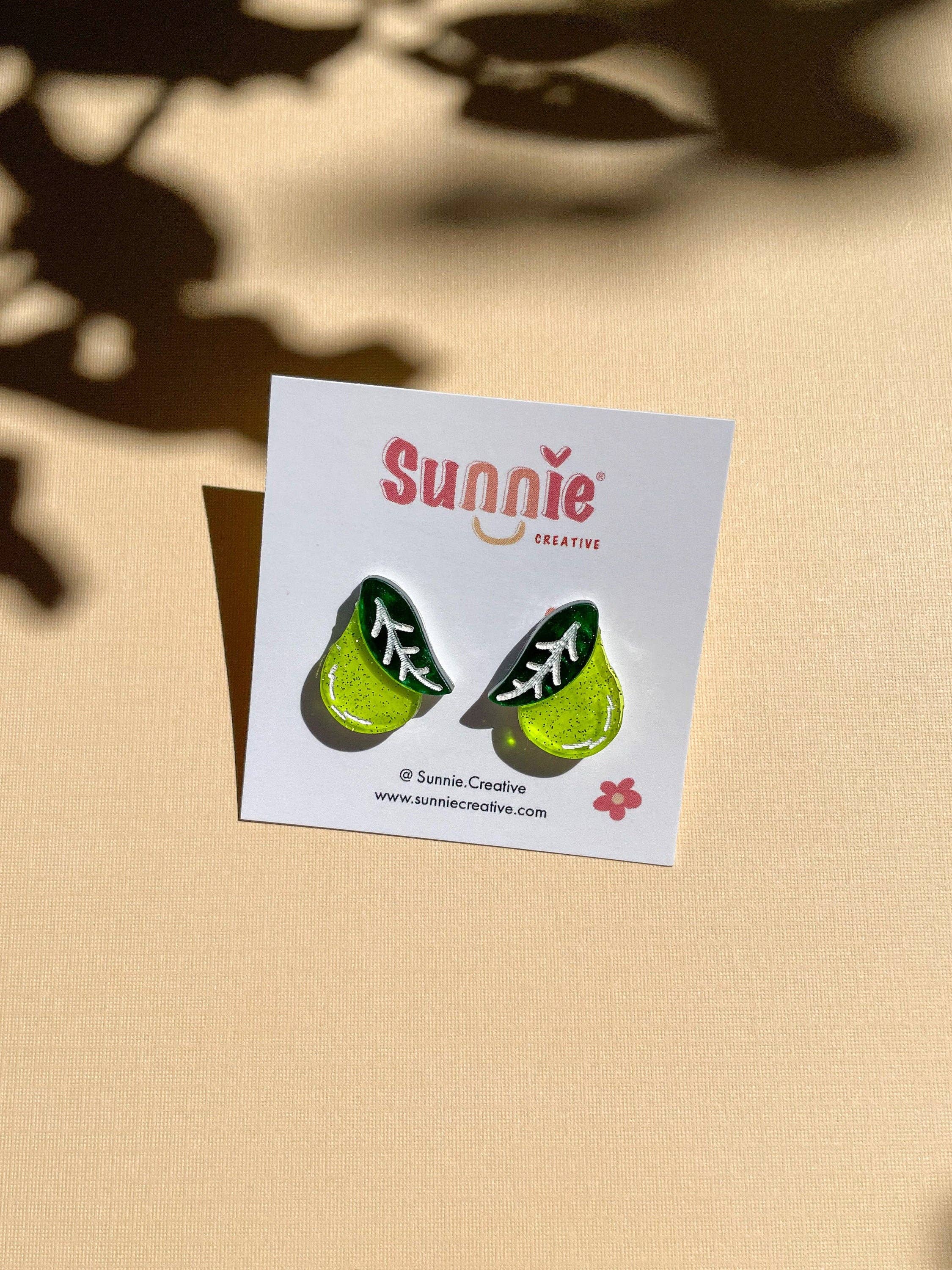 Mini Pear Dangle earrings by Sunnie Creative displayed on a light background, showcasing a unique handmade design featuring a green pear shape with leaf detail.