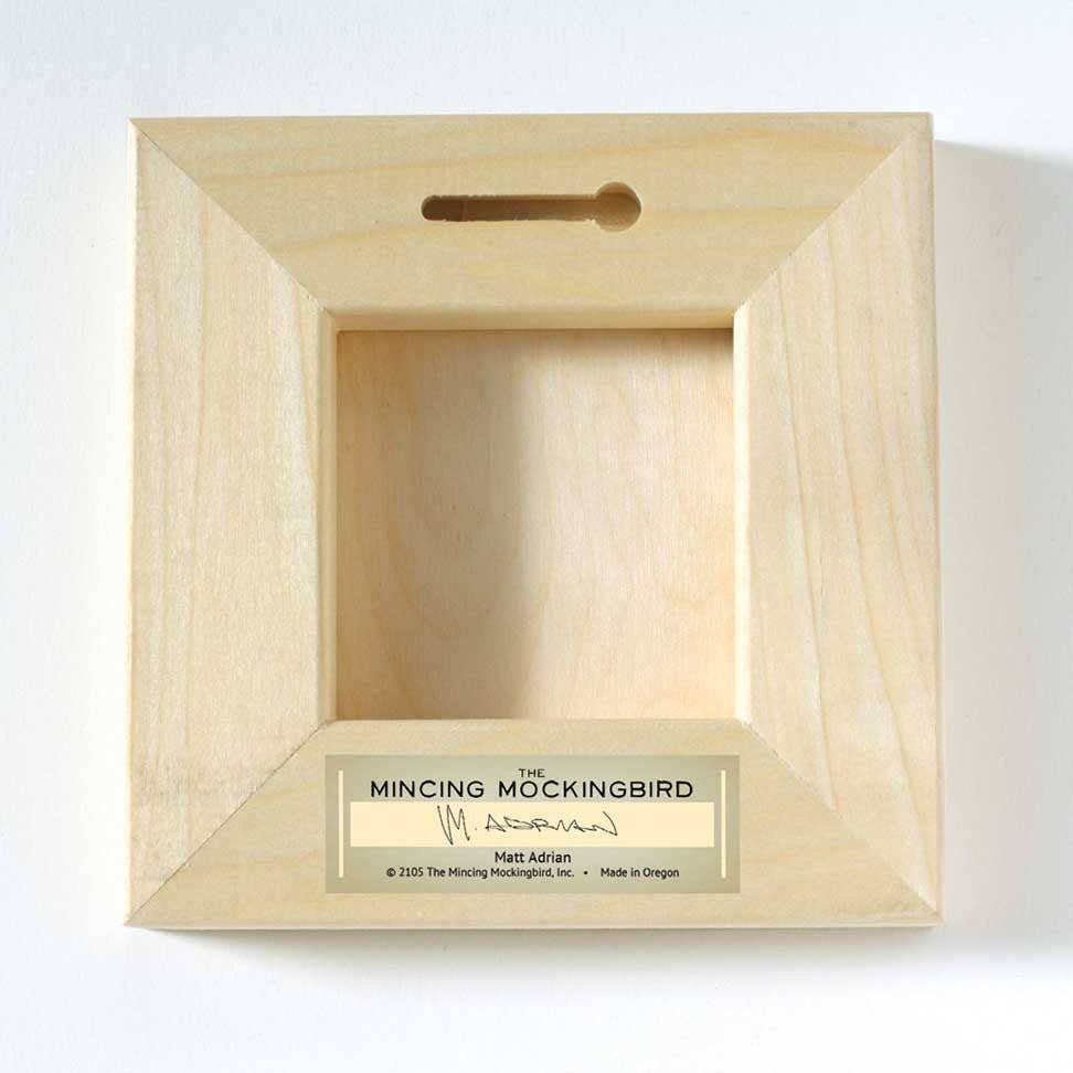 Wooden frame with a label 'the mincing mockingbird'