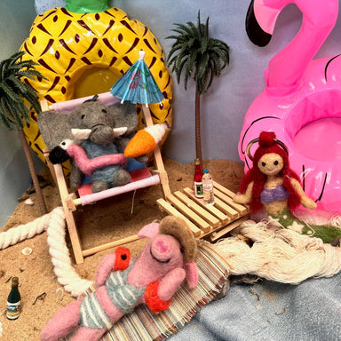 Felt ornaments with pineapple chair, elephant, pink flamingo on a sandy surface.