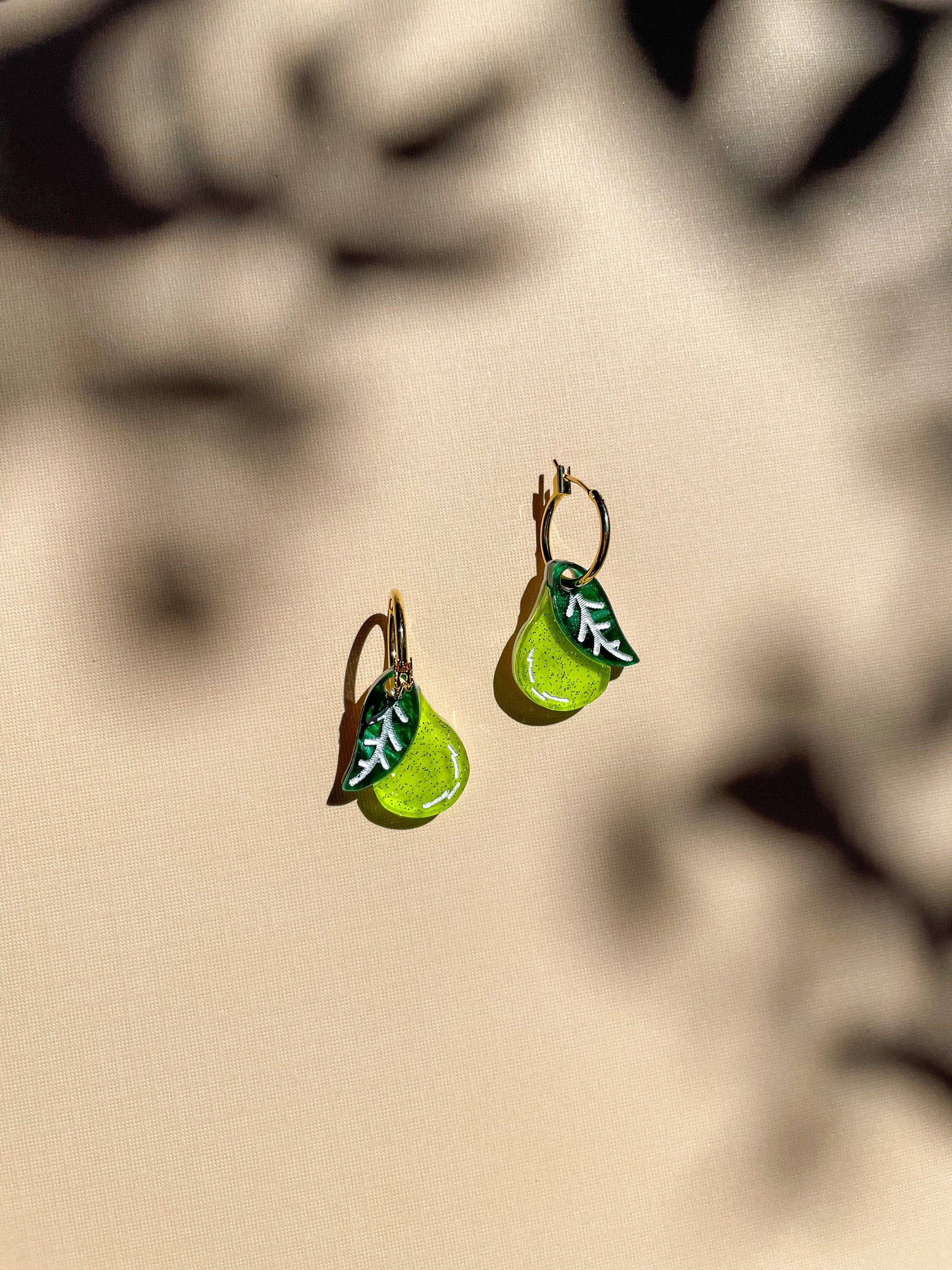 Mini Pear Dangle earrings by Sunnie Creative, showcasing a vibrant green acrylic design with a leaf detail, elegantly hanging against a softly lit background.