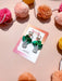 Bok Choy Dangle earrings by Sunnie Creative presented on a card surrounded by colorful pom poms, emphasizing their playful and artistic style.