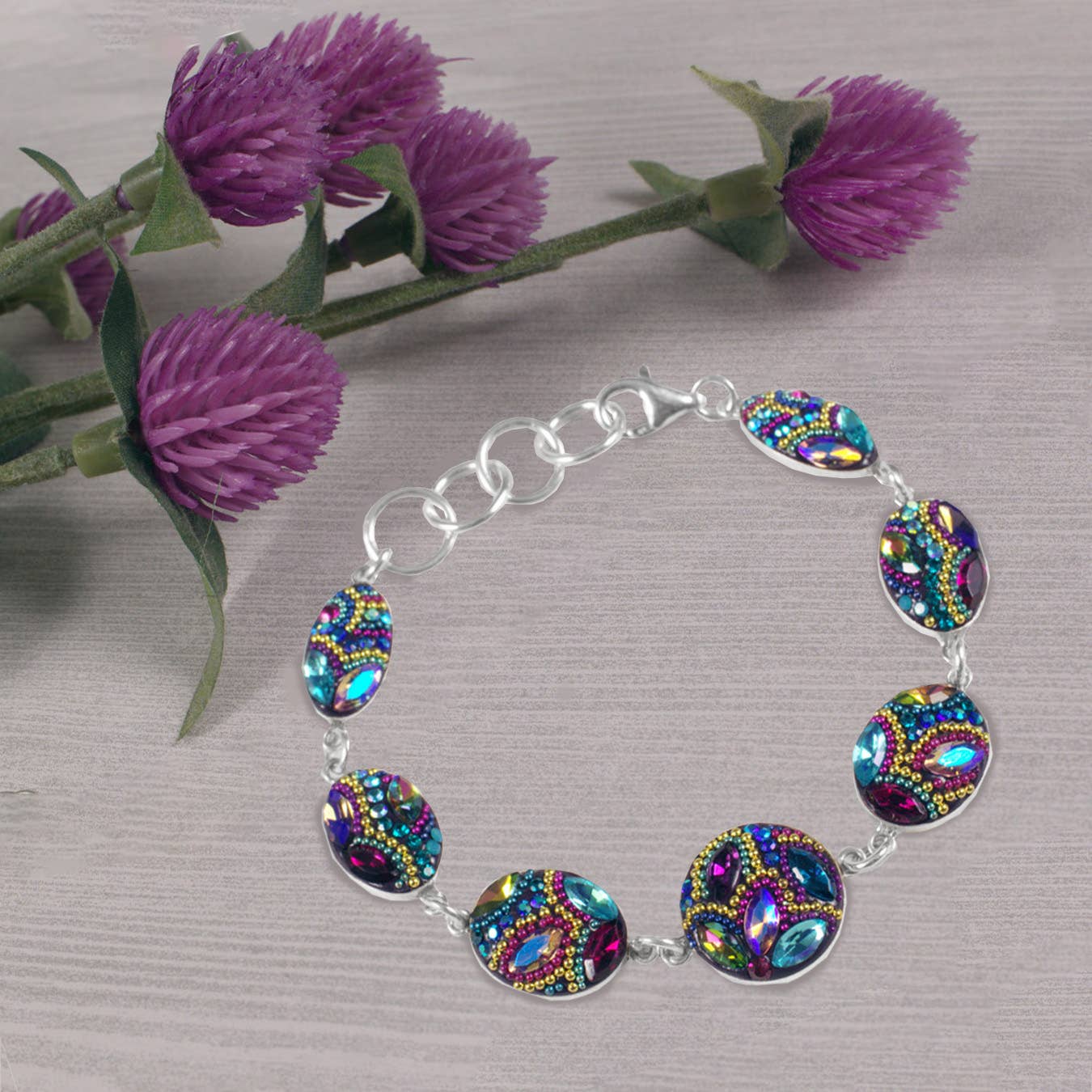 Edgeless Bracelet by Mosaico Jewels displayed with purple flowers, highlighting its unique design with striking colored beads on a silver chain.