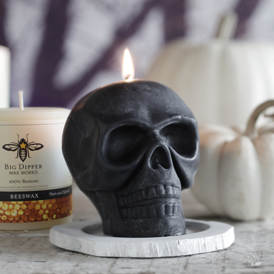 Black skull-shaped candle with a lit wick on a wooden surface