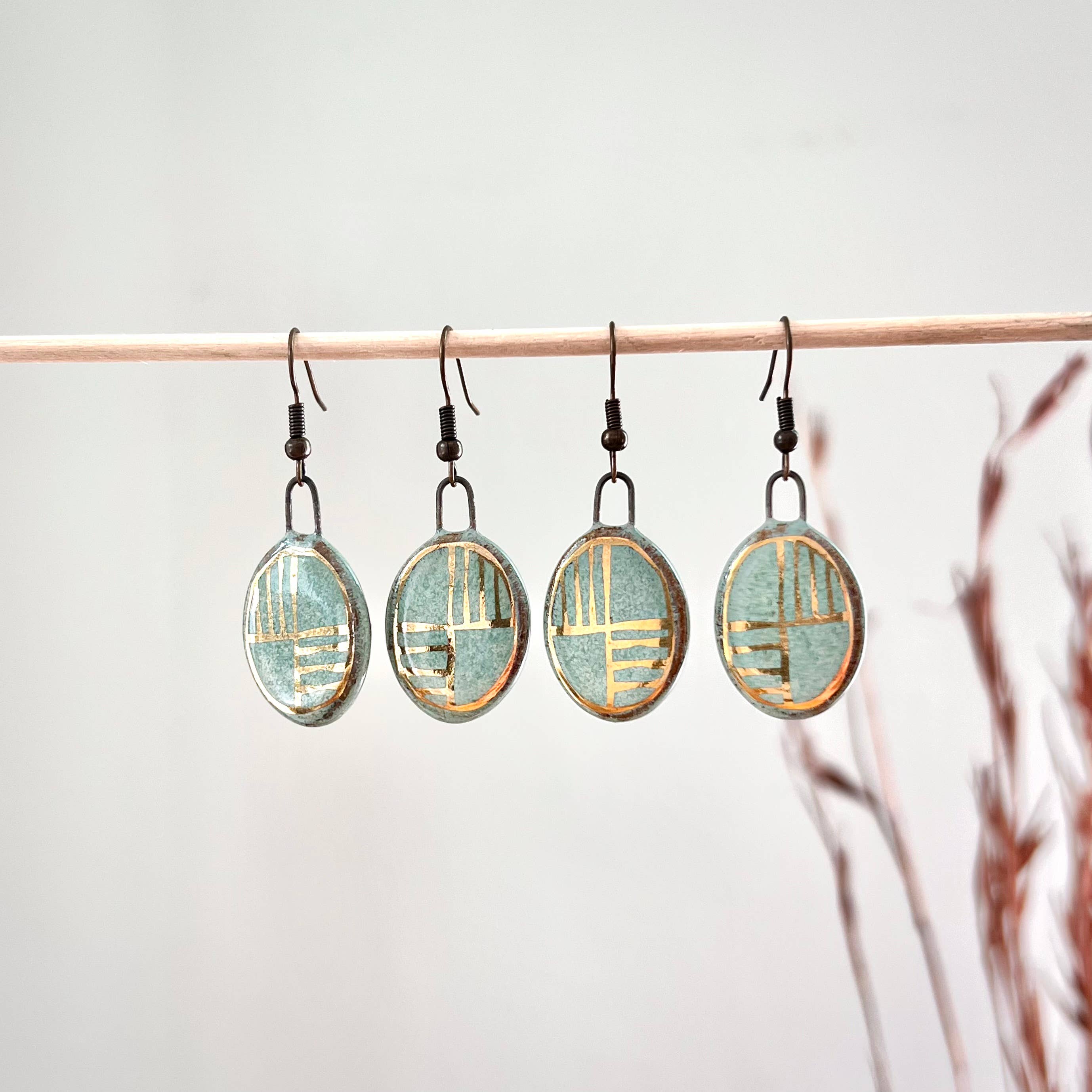 Multiple pairs of Turquoise Oval Earrings with Gold Checkered Lines hanging on a display, showcasing the elegant design by The Artifact House.