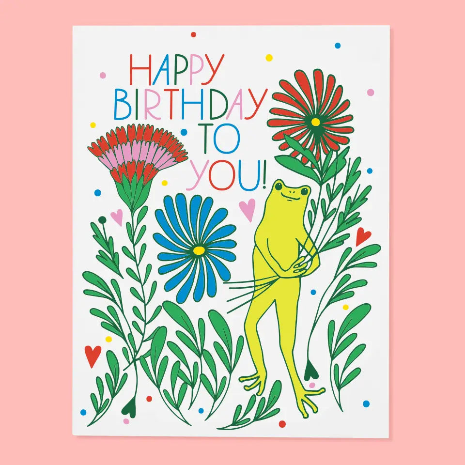 Cheerful birthday card showing a bright yellow frog among colorful flowers with the text 'HAPPY BIRTHDAY TO YOU!' from The Good Twin Card Collection, designed by The Good Twin.