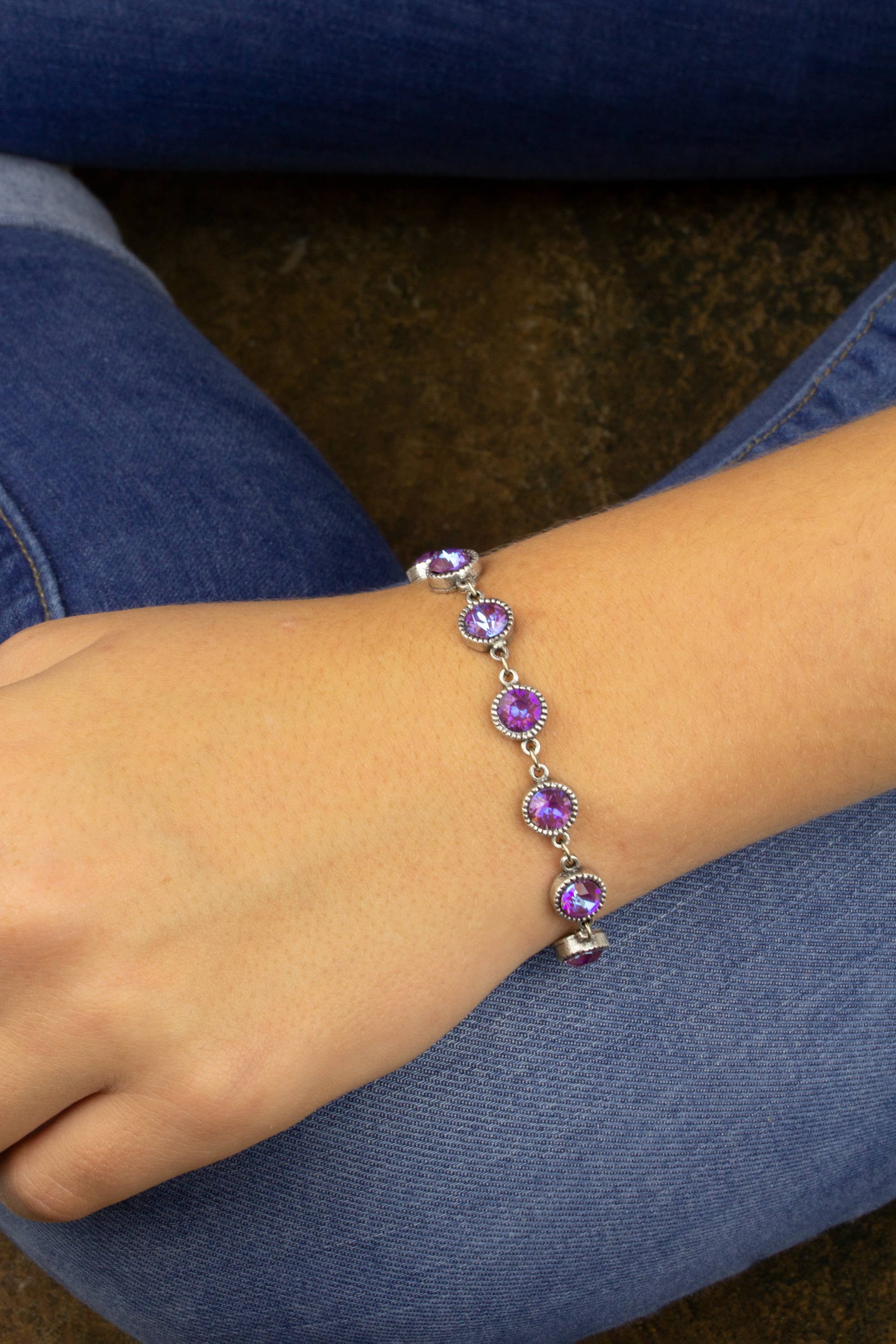 Bracelet with purple gemstones on a wrist, wearing blue jeans.