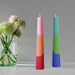 Colorful Decorative Fluted Taper Candles by Made By Humans, featuring a bold three-color pattern in pink, orange, and vibrant green, placed next to a clear vase with flowers.