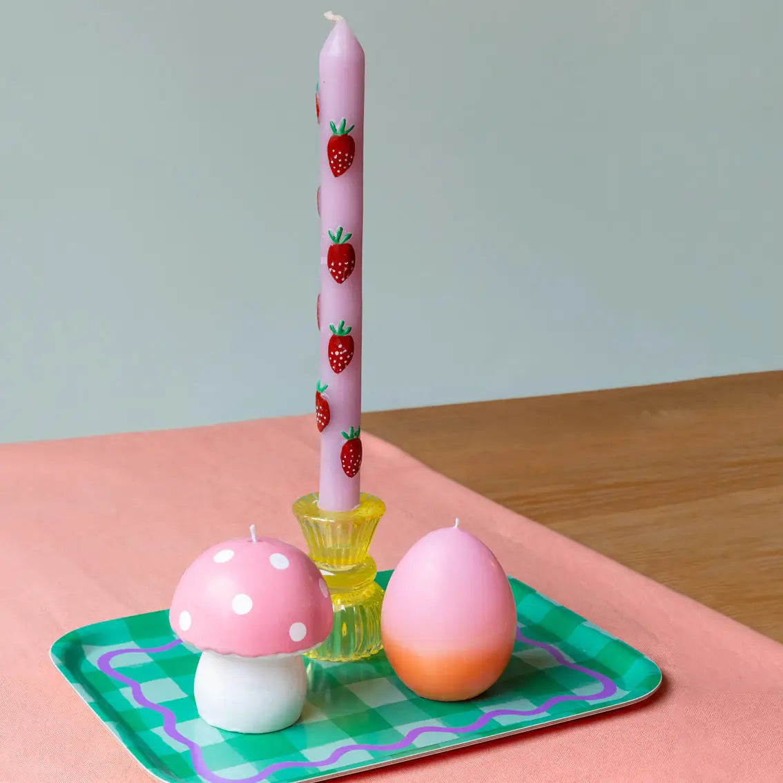 Pastel pink dinner candle with strawberry design from Talking Tables USA, displayed on a colorful table with additional decorative candles.