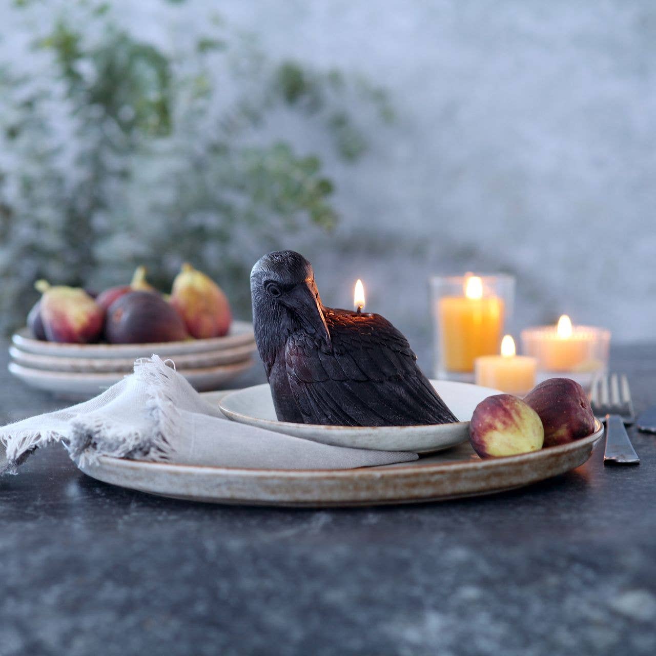 Decorative bird-shaped candle on a plate with figs and candles