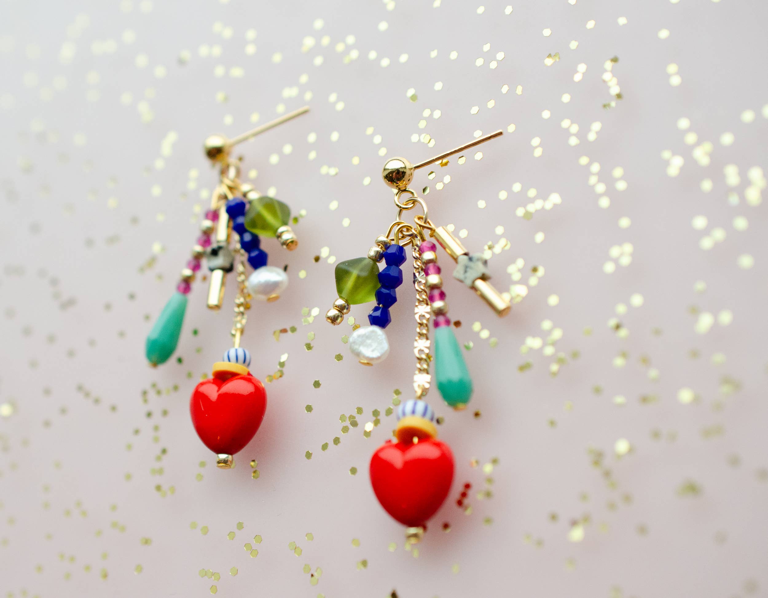 Colorful Heart Charm Earrings by Jill Makes, featuring a variety of glass, acrylic, and Czech beads, with red heart charms, hanging elegantly against a sparkling background.