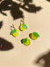 Mini Lemon Dangle earrings displayed on a textured background with shadow play, featuring vibrant yellow acrylic with green leaf accents by Sunnie Creative.