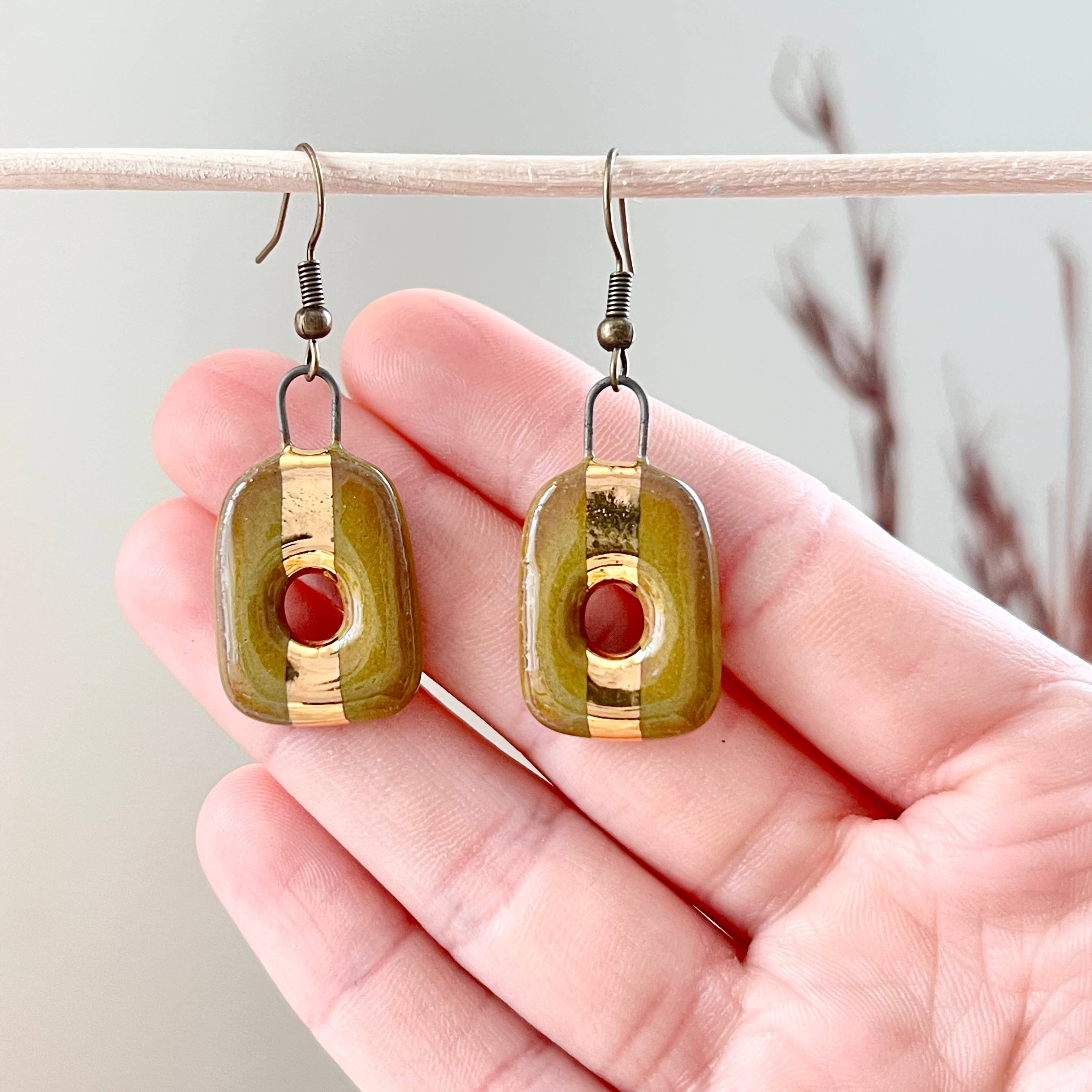 Olive Square Loop Ceramic Stoneware Earrings showcased being held in a hand, featuring a unique design with 24K gold detailing by The Artifact House.