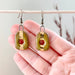Olive Square Loop Ceramic Stoneware Earrings showcased being held in a hand, featuring a unique design with 24K gold detailing by The Artifact House.