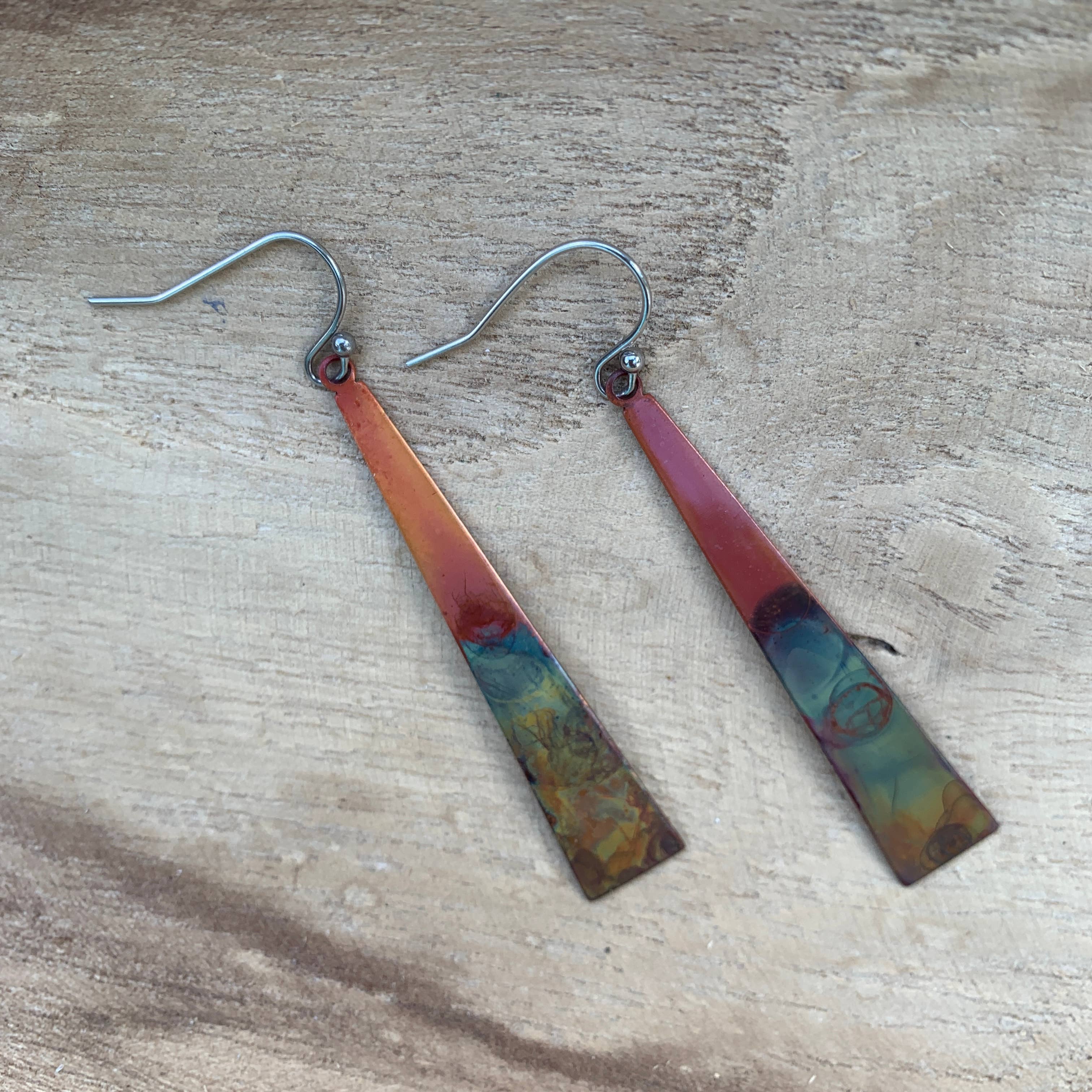 Stylish triangle stick earrings by Positive Shine Jewelry, featuring unique colors and designs, hanging from stainless steel wires, perfect for any outfit.