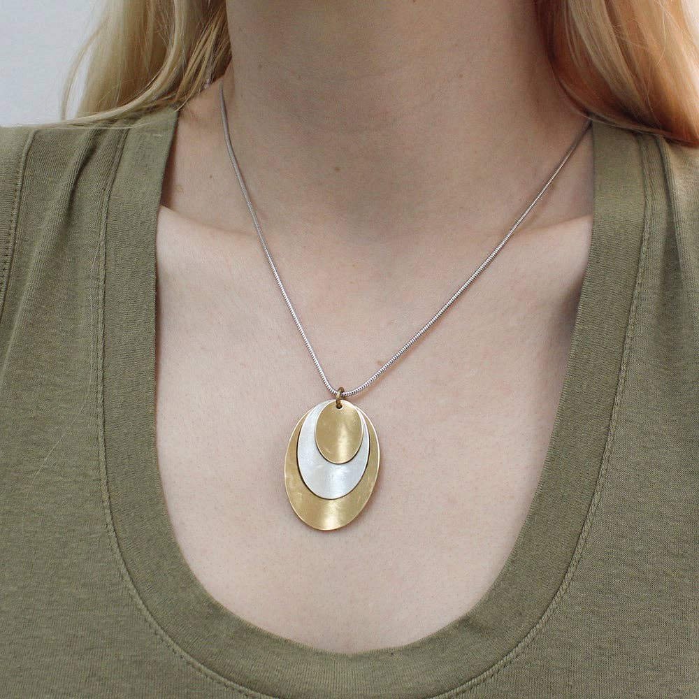 Close-up of Layered Dished Ovals Necklace in brass and silver, highlighting its sculptural form and adjustable lobster claw closure.