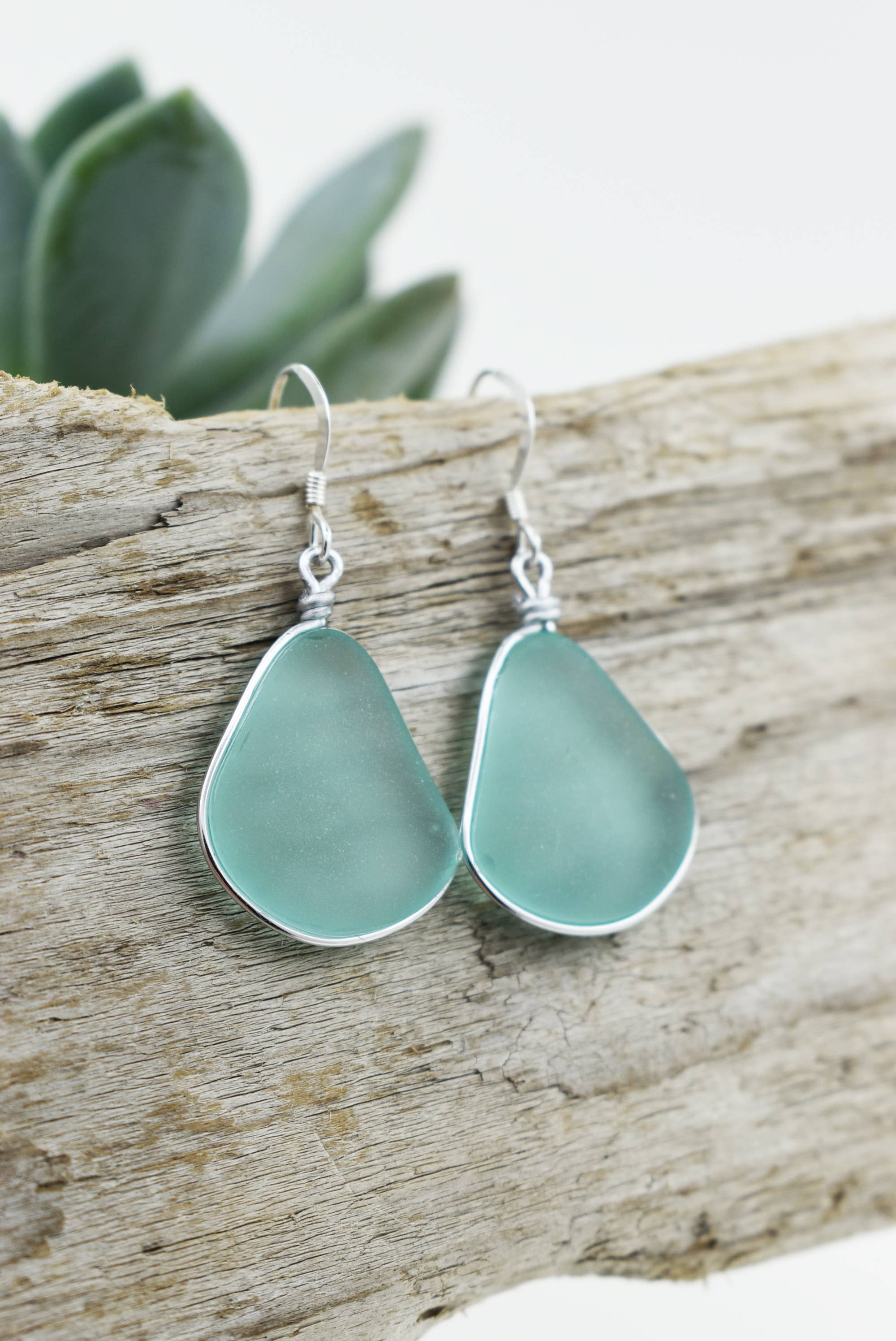 Flat lay of Eco Glass Bezel Drop Silver Earrings: Aqua with a beach-inspired background, emphasizing their coastal elegance.