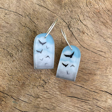 Blue Skies Earrings by Fernworks featuring a tiny hand-painted scene of birds in calm blue skies, made from acrylic, ink, layered resin, and wood, with silver ear wires.