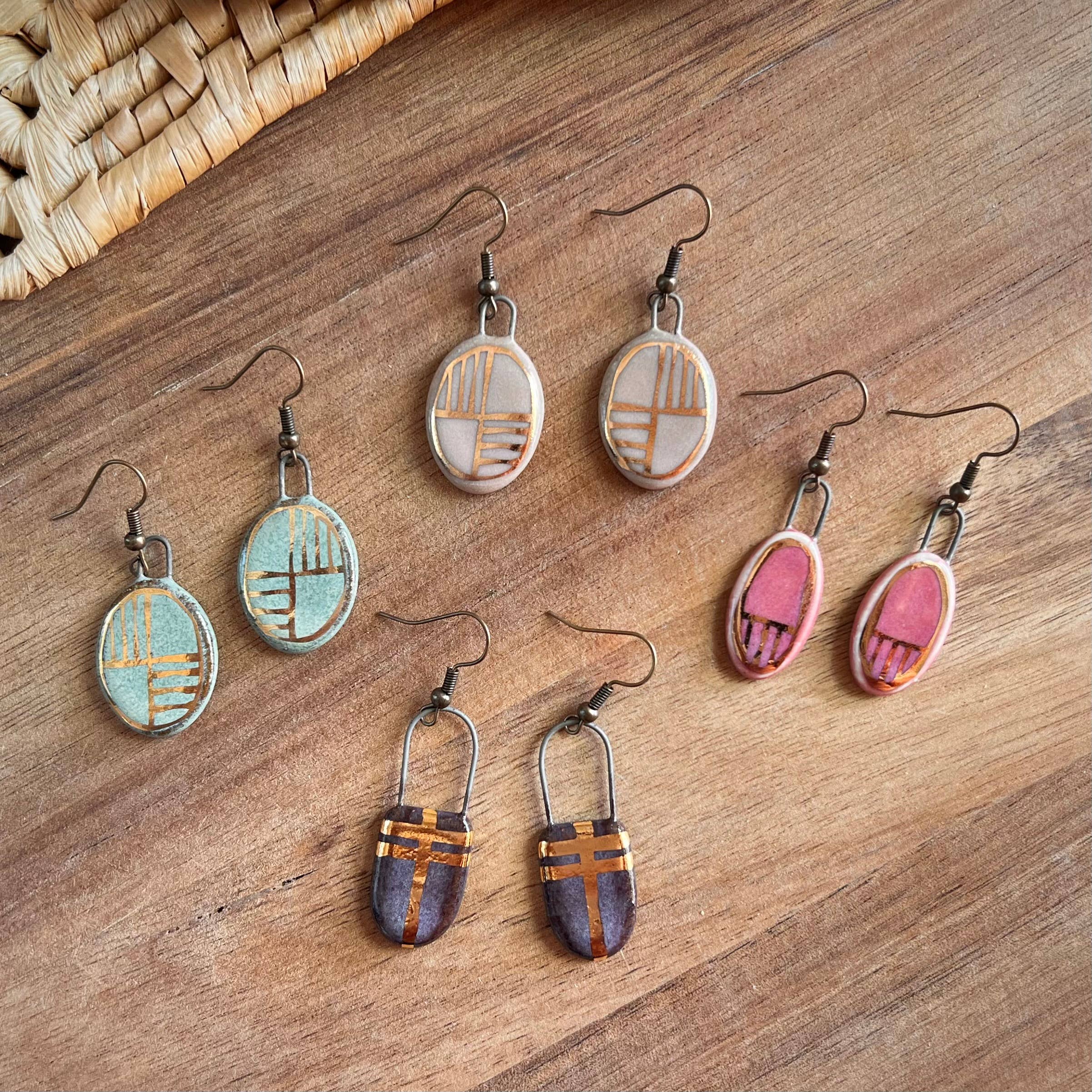 A collection of Turquoise Oval Earrings with Gold Checkered Lines alongside other colorful earrings, highlighting the handmade elegance from The Artifact House.