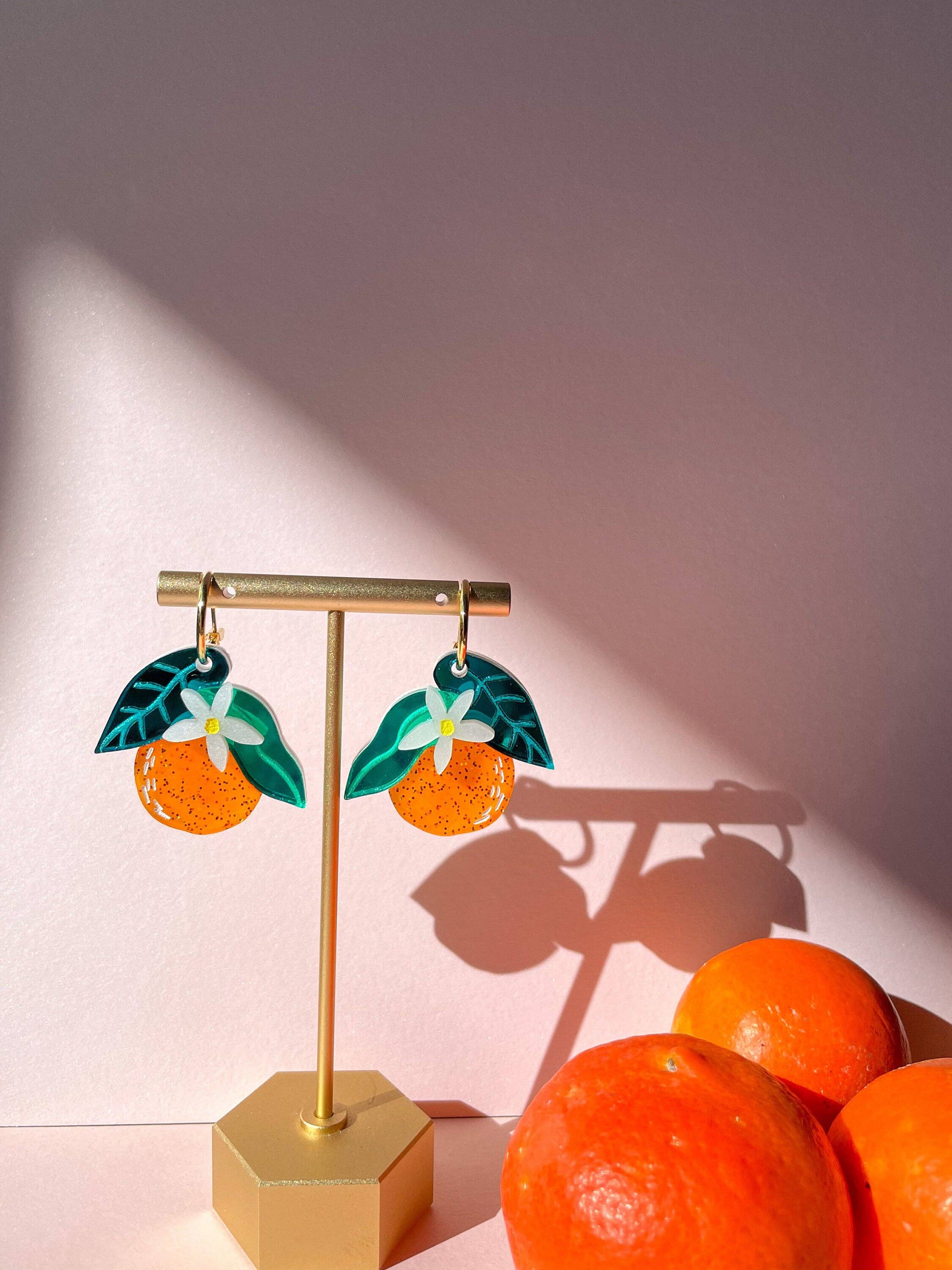 Stylish Orange Dangle earrings presented on a display stand with oranges, highlighting the intricate design and bright colors crafted by Sunnie Creative.