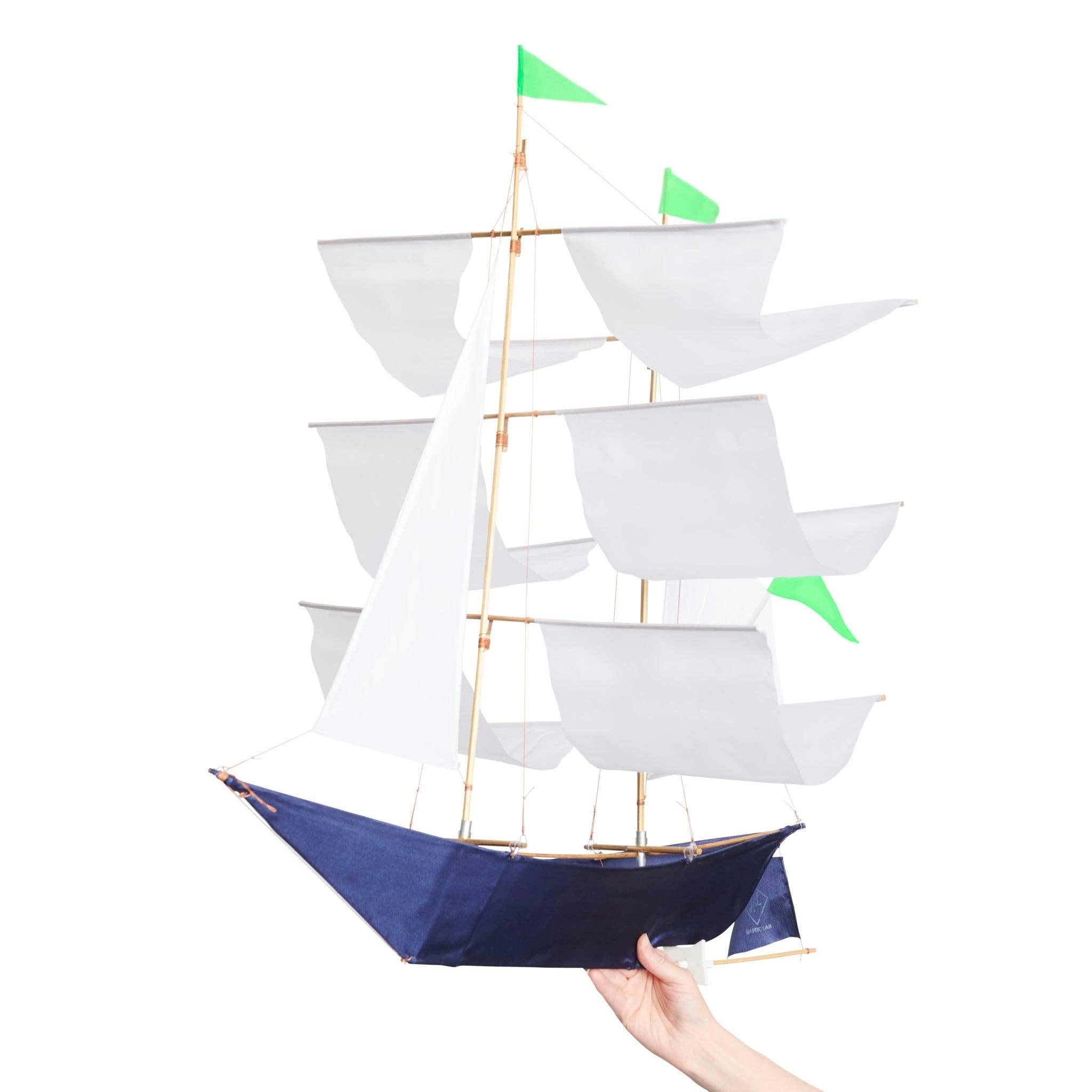 Dark navy blue and white Sailing Ship Kite by Haptic Lab, held by a person, highlighting its craftsmanship and unique appearance.
