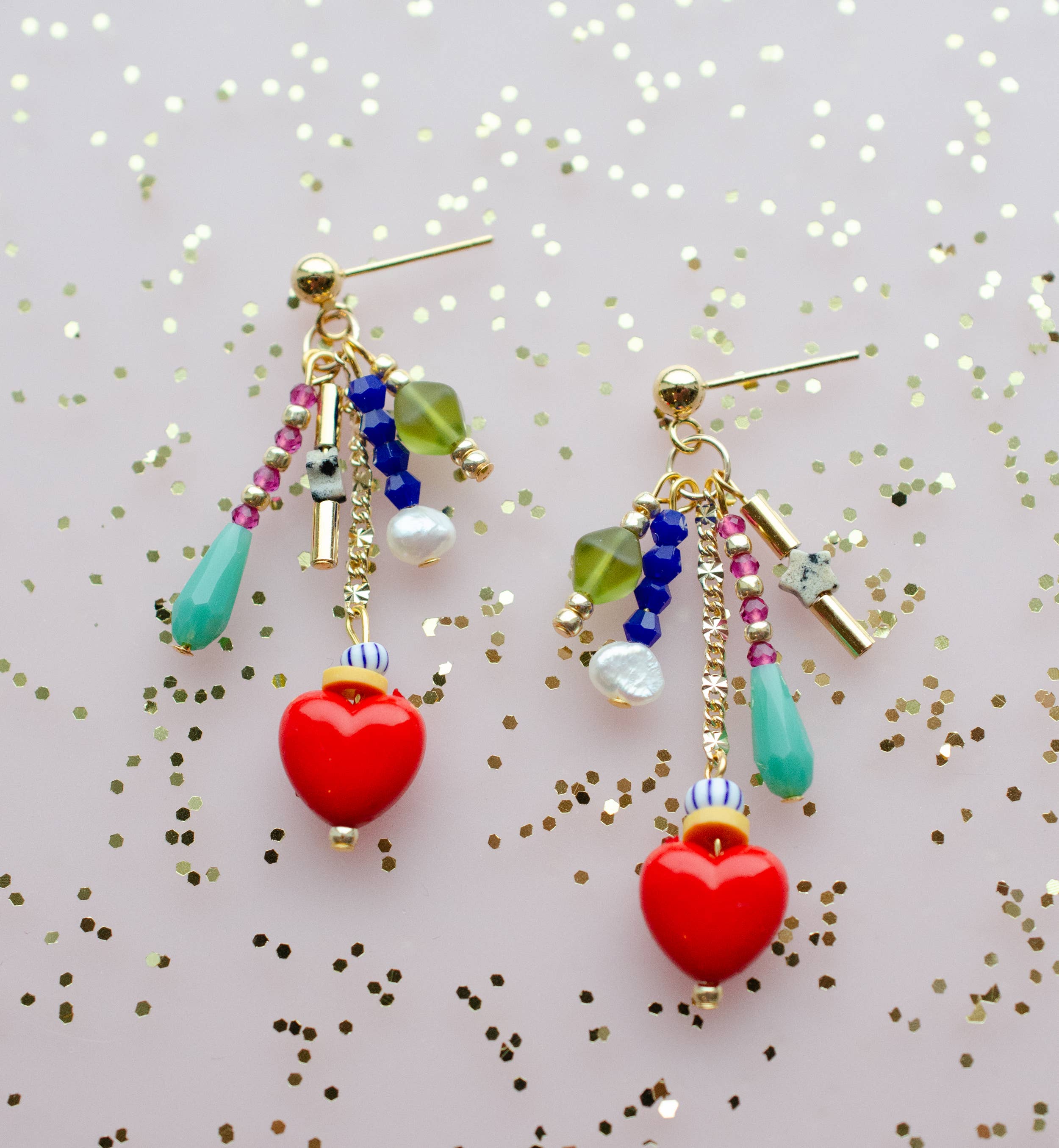 Close-up view of the Heart Charm Earrings by Jill Makes, showcasing the vibrant assortment of beads and the red heart charms, set against a shimmery backdrop.
