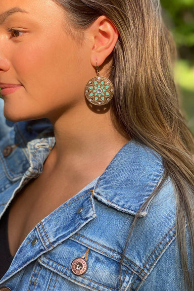 Close-up of a person wearing a floral earring with a denim jacket.