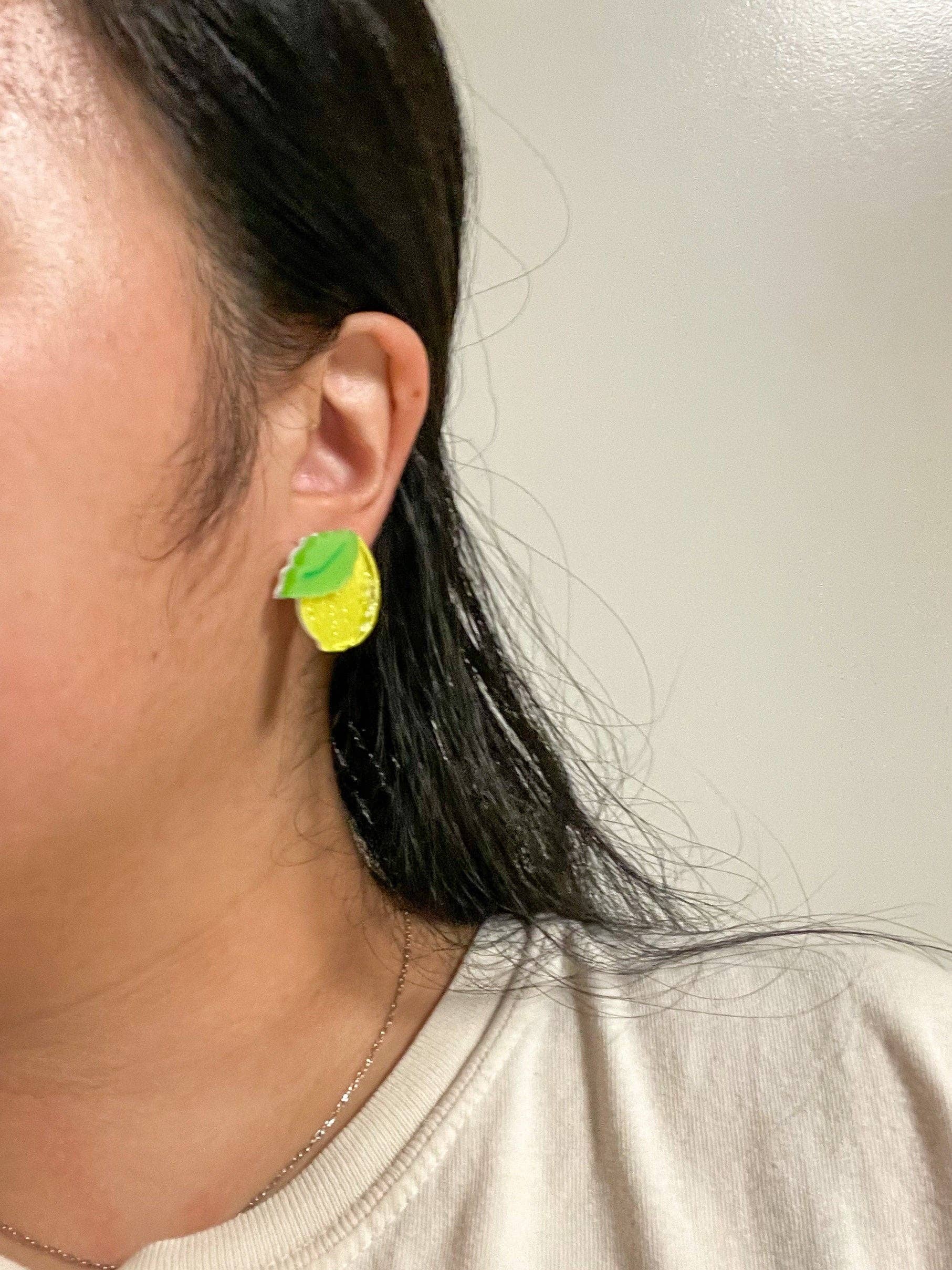 Close-up of a person wearing Mini Lemon Dangle earrings, featuring the bright yellow acrylic and green leaf design by Sunnie Creative.